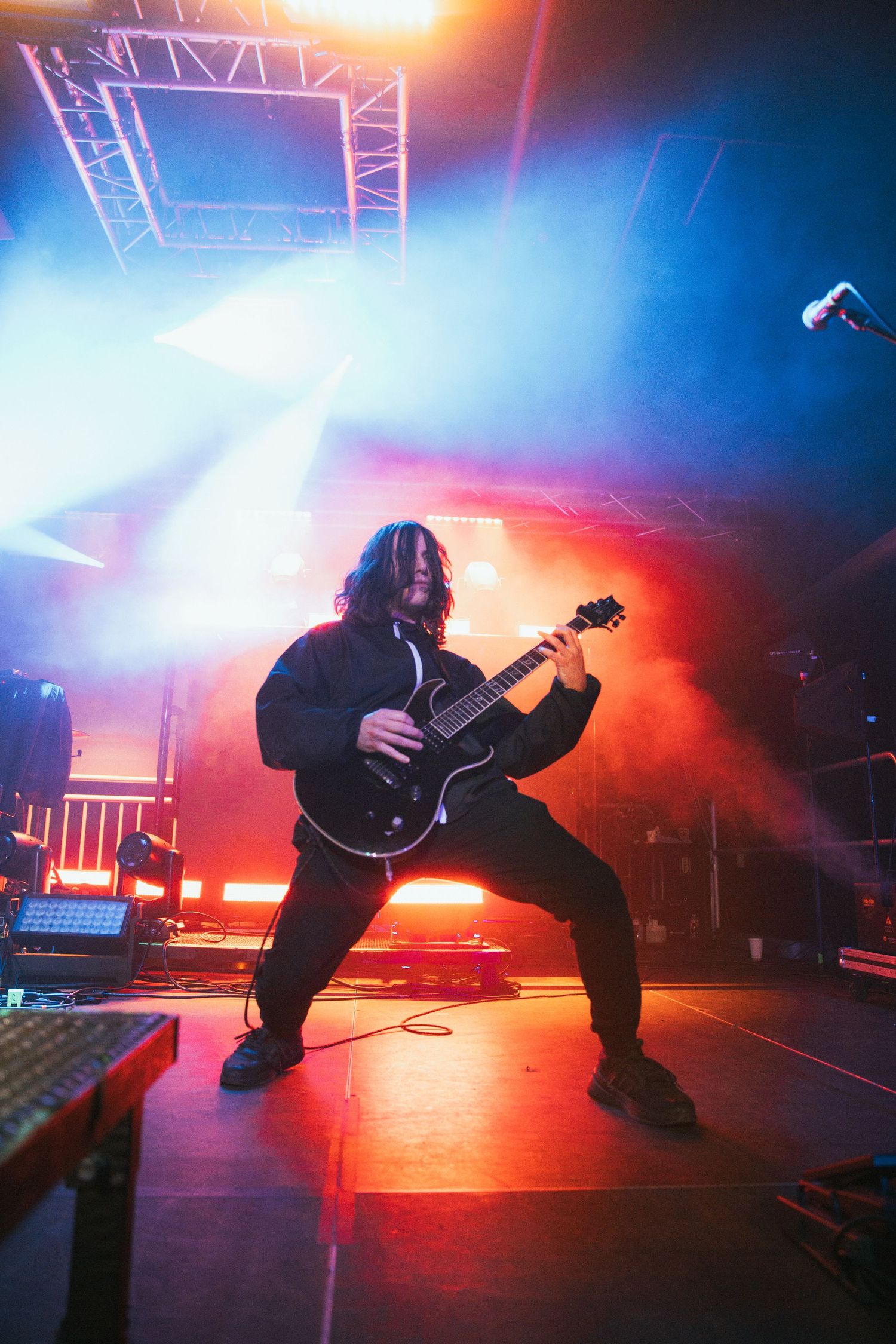 Silhouetted guitarist performs on stage with dramatic red and blue lighting effects during a live concert performance.
