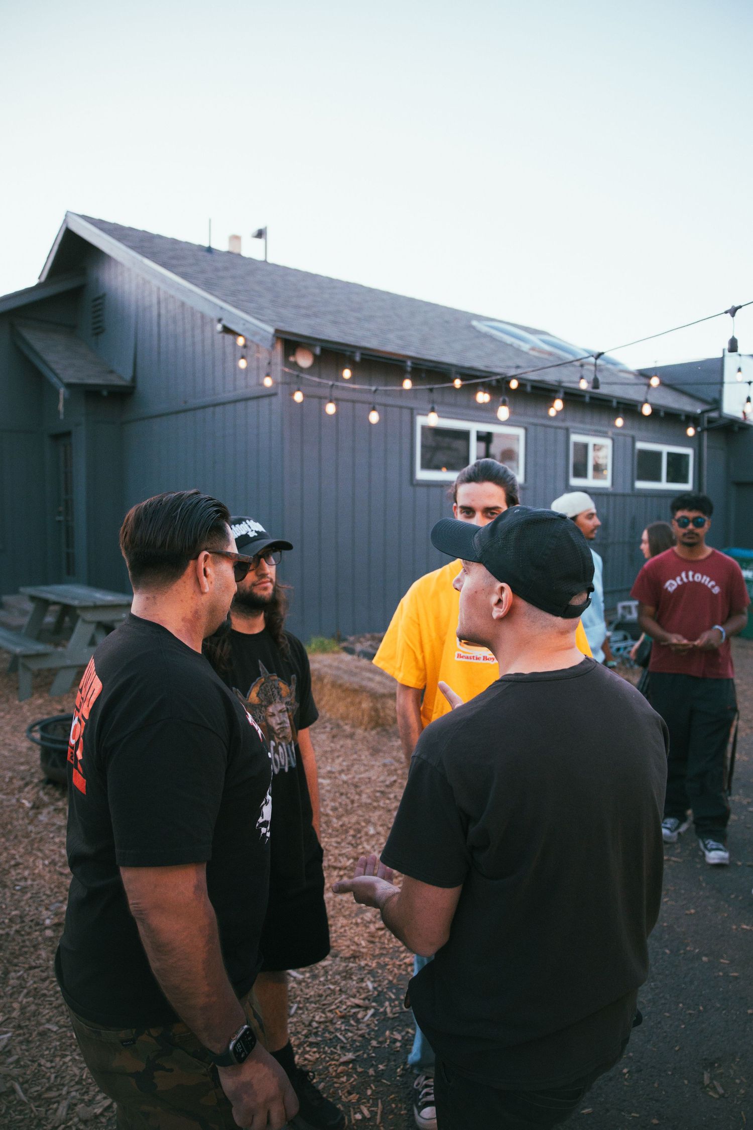 Group of people gathered outside a gray house with string lights at dusk.