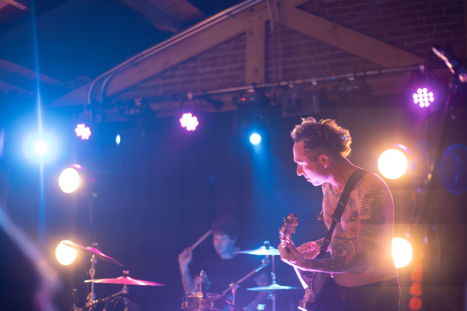 Musician plays drums on stage surrounded by colorful spotlights.
