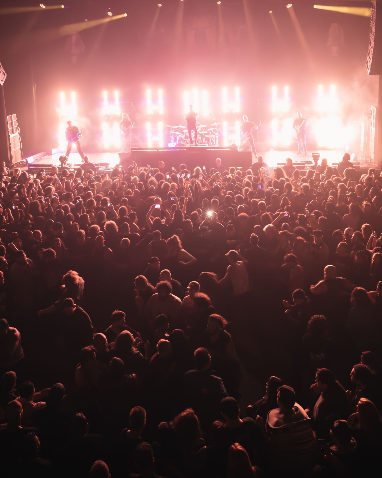 A massive crowd enjoys a live concert with dramatic pink stage lighting illuminating performers on stage.