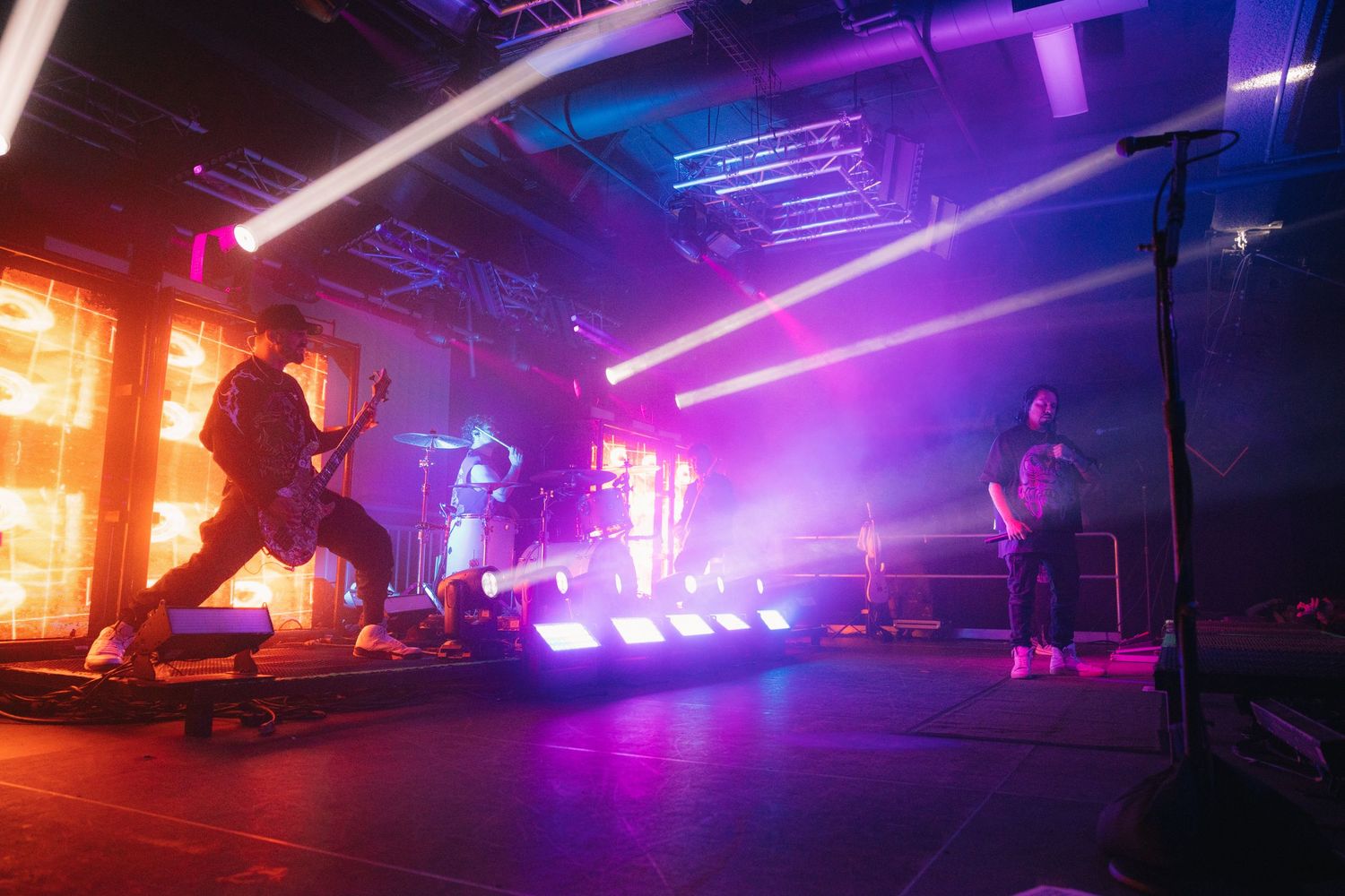 Silhouetted performers on stage with vibrant purple and orange lighting effects during a dynamic live concert performance.