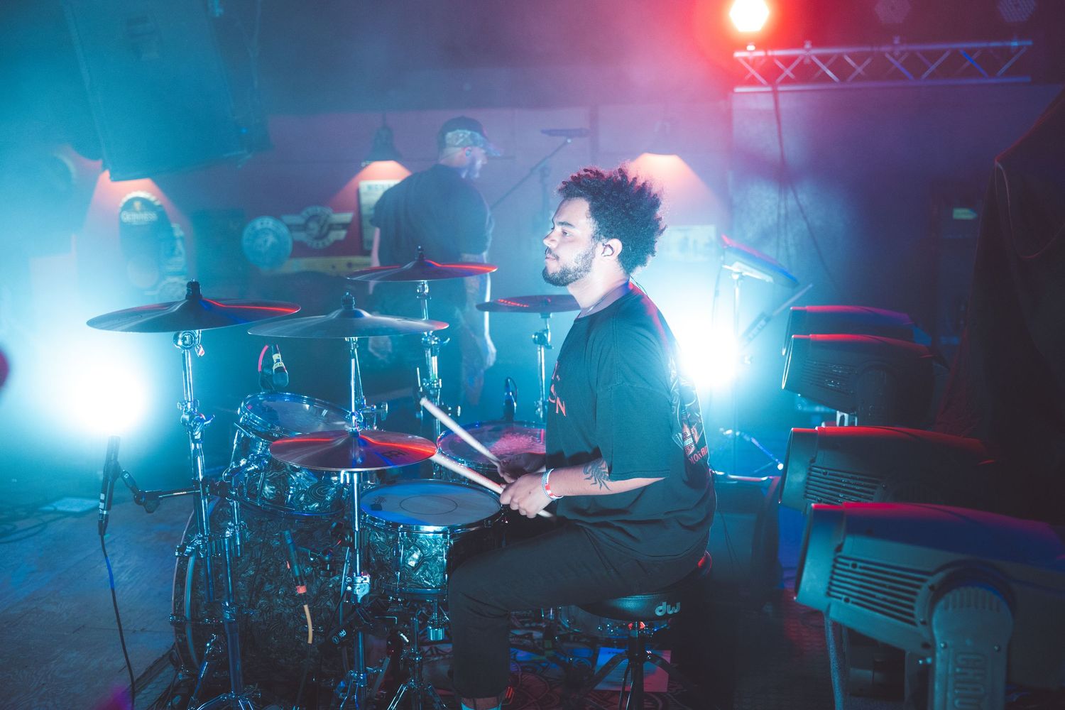 Musicians perform at a concert with dramatic red and blue lighting on a stage filled with fog.