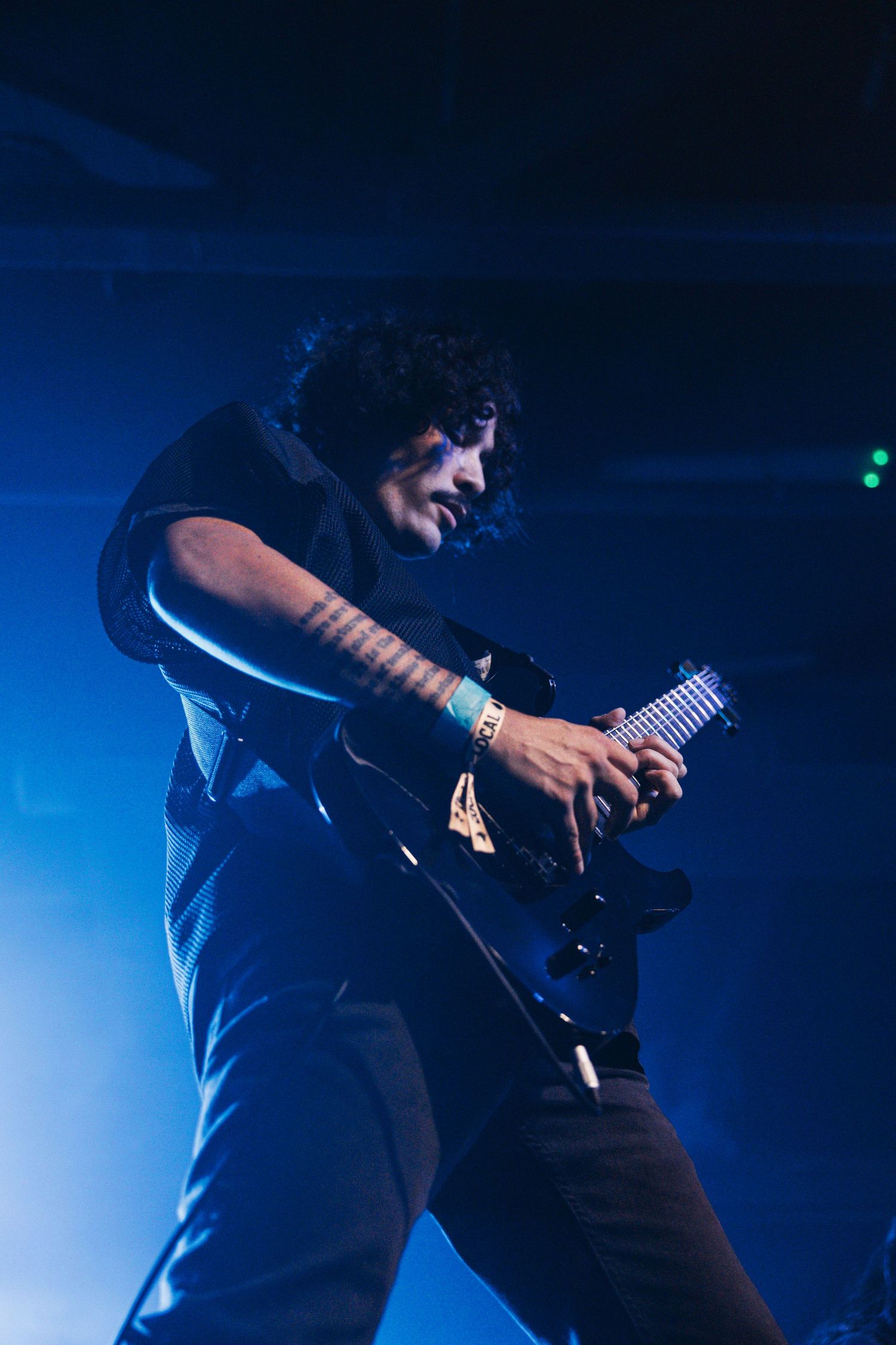 Silhouetted guitarist performs on darkened stage with dramatic blue lighting during live concert performance.