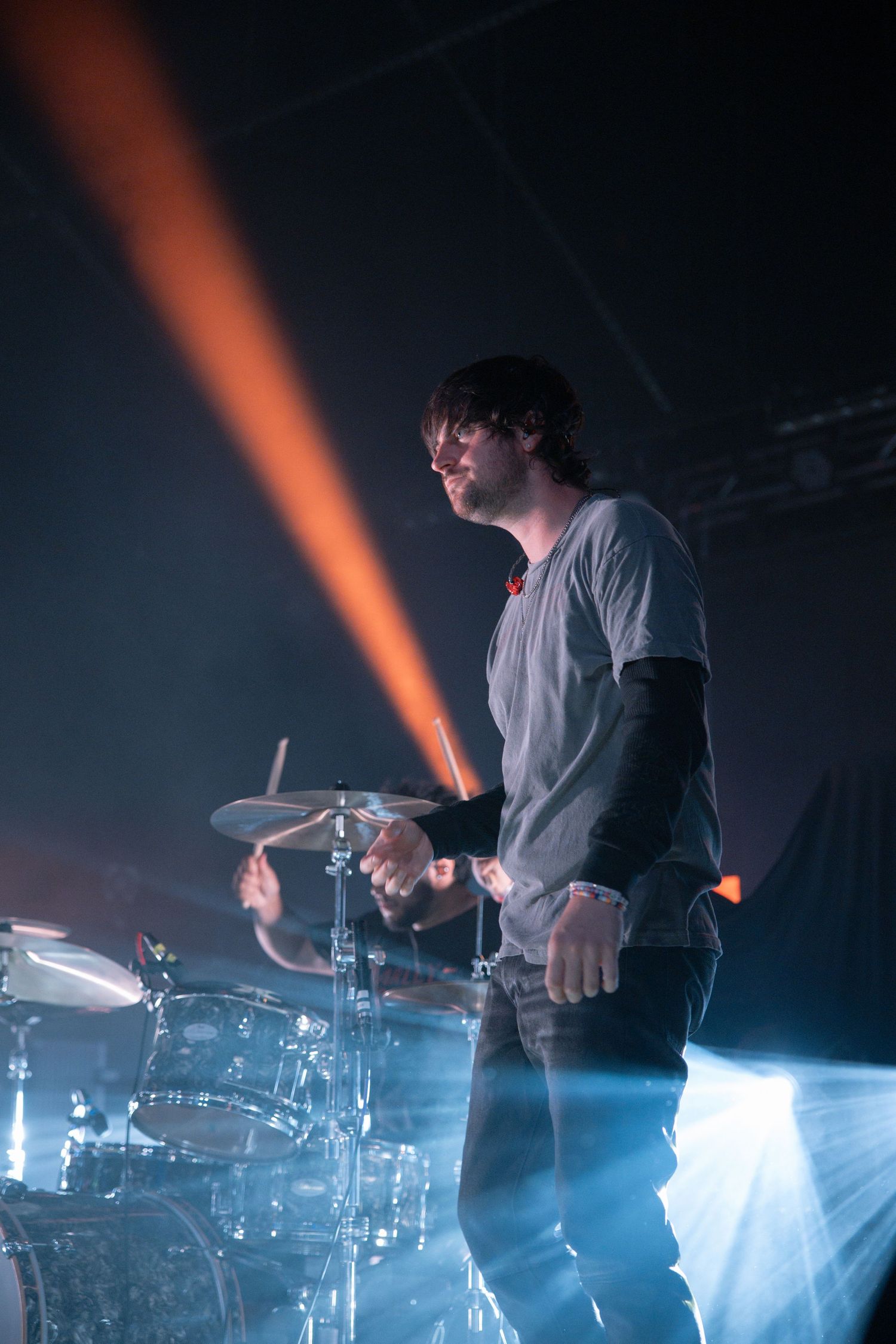 A drummer performs on stage with dramatic orange and blue lighting effects during a concert.