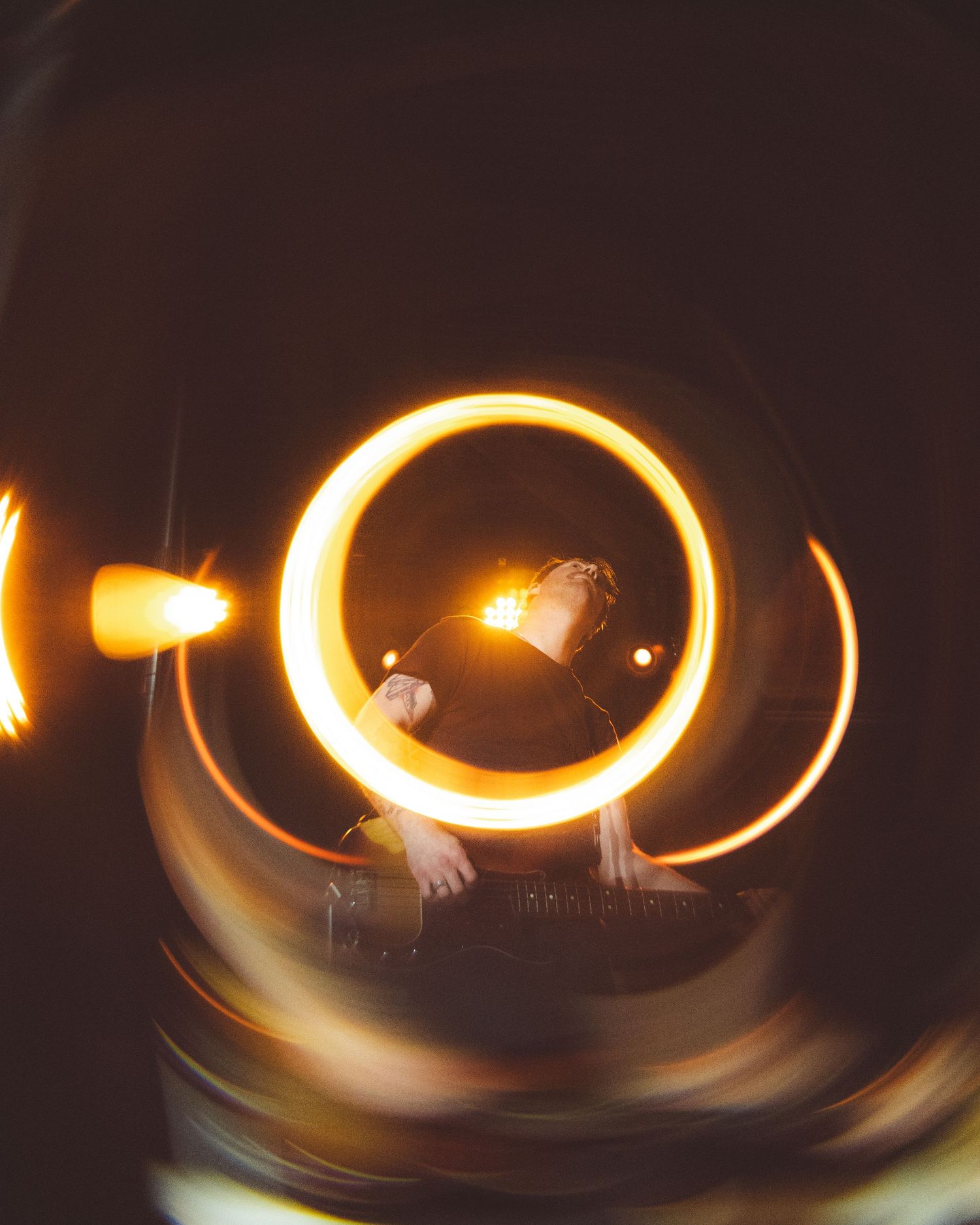 Long exposure light painting creates glowing orange circular trails in dark environment.