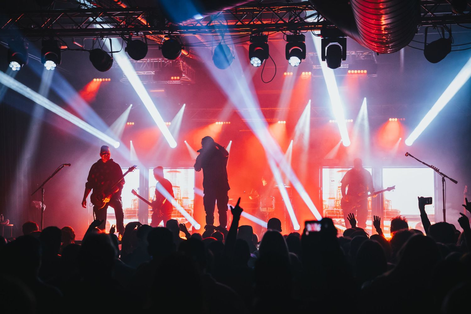 Silhouetted performers on stage with dramatic red and white spotlights during an energetic concert performance.