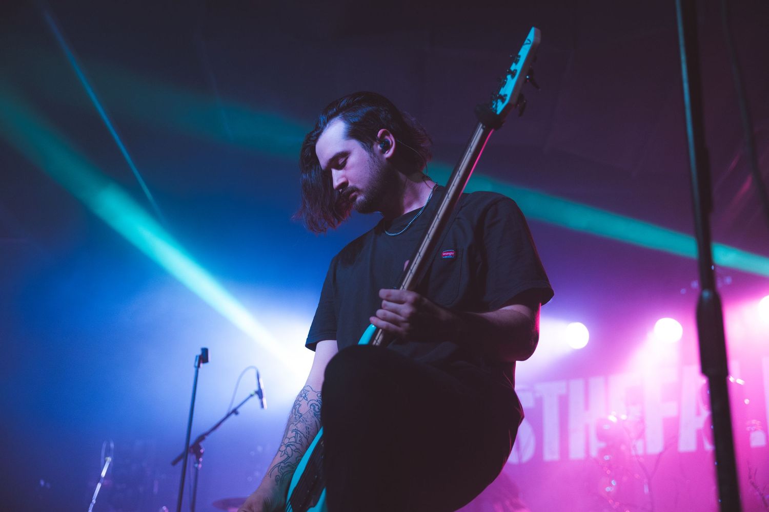 A musician performs on stage with electric guitar silhouetted against dramatic blue and purple concert lighting.