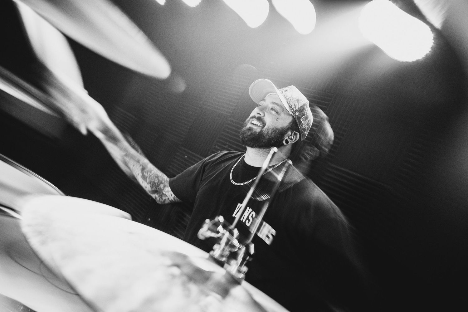 Black and white photo of a male drummer performing live on stage under dramatic spotlights.