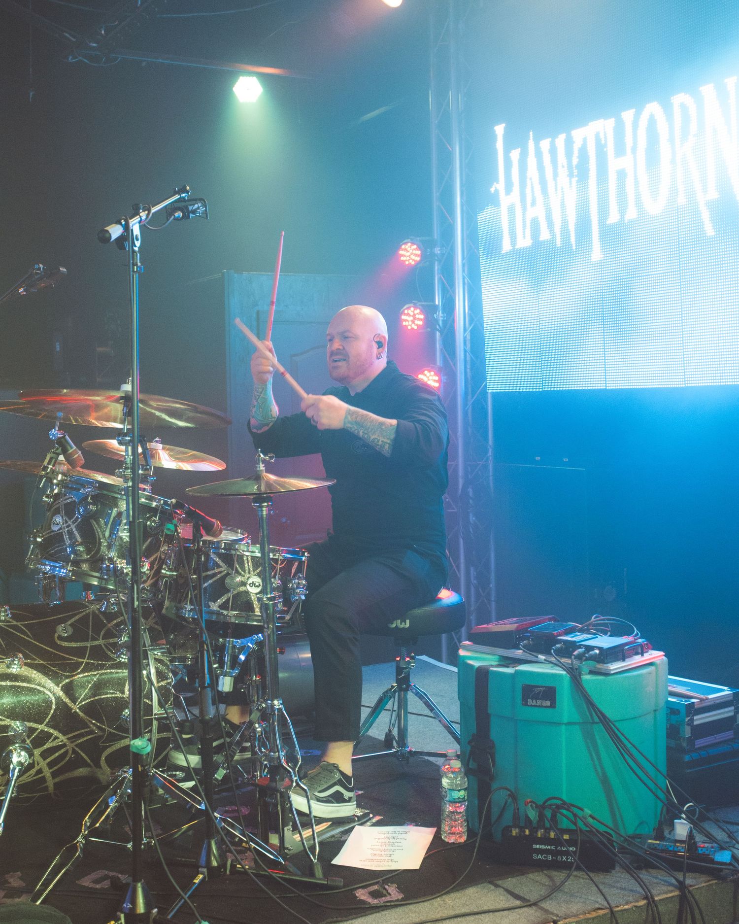 Drummer performing behind extensive drum kit with Hawthorn signage visible in background.