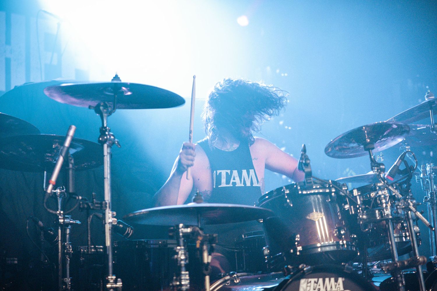 Concert stage with drum kit and cymbals illuminated by ethereal blue stage lighting effects.