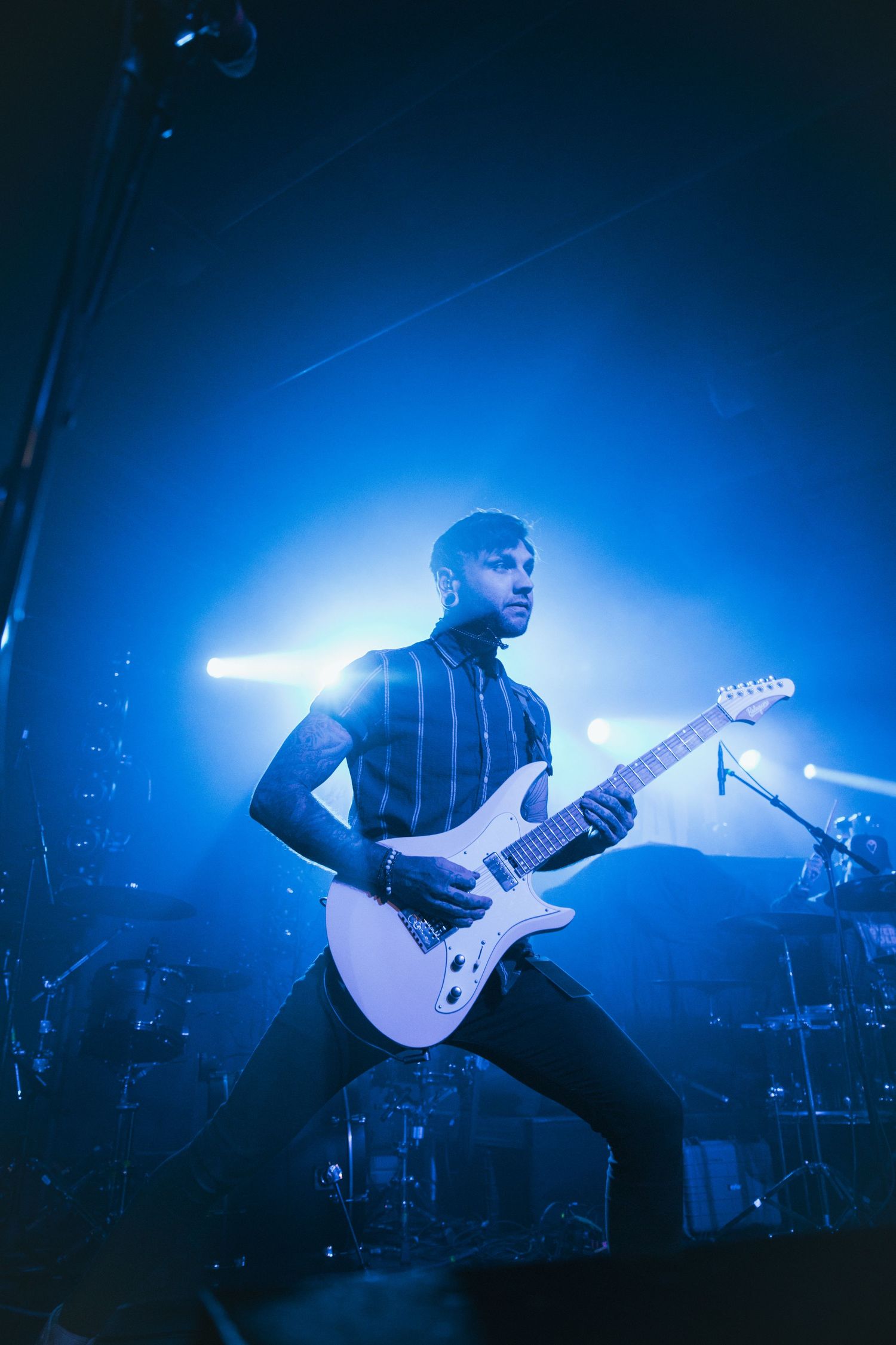 A guitarist performs on stage bathed in dramatic blue concert lighting with multiple silhouetted shots showing their movement.