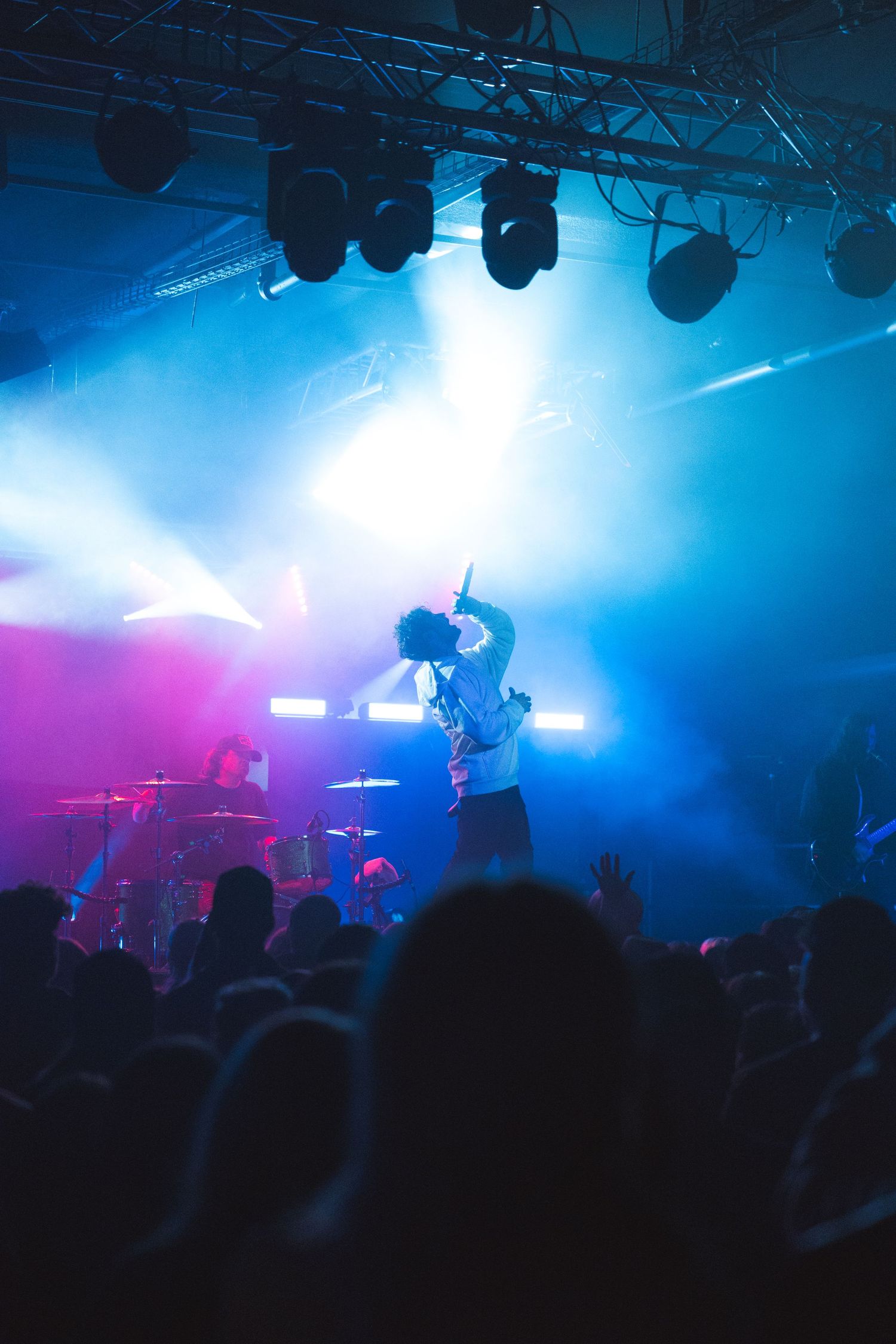 Concert performer silhouetted on stage with dramatic blue and pink lighting while crowd watches in dark venue.