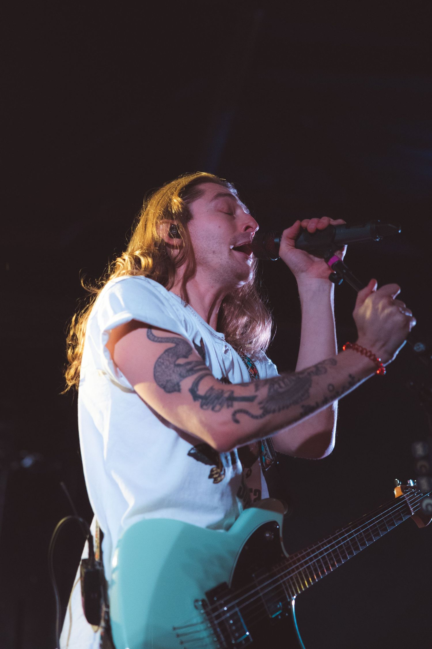 A musician in a white shirt performs passionately on stage, singing into a microphone with dramatic lighting.