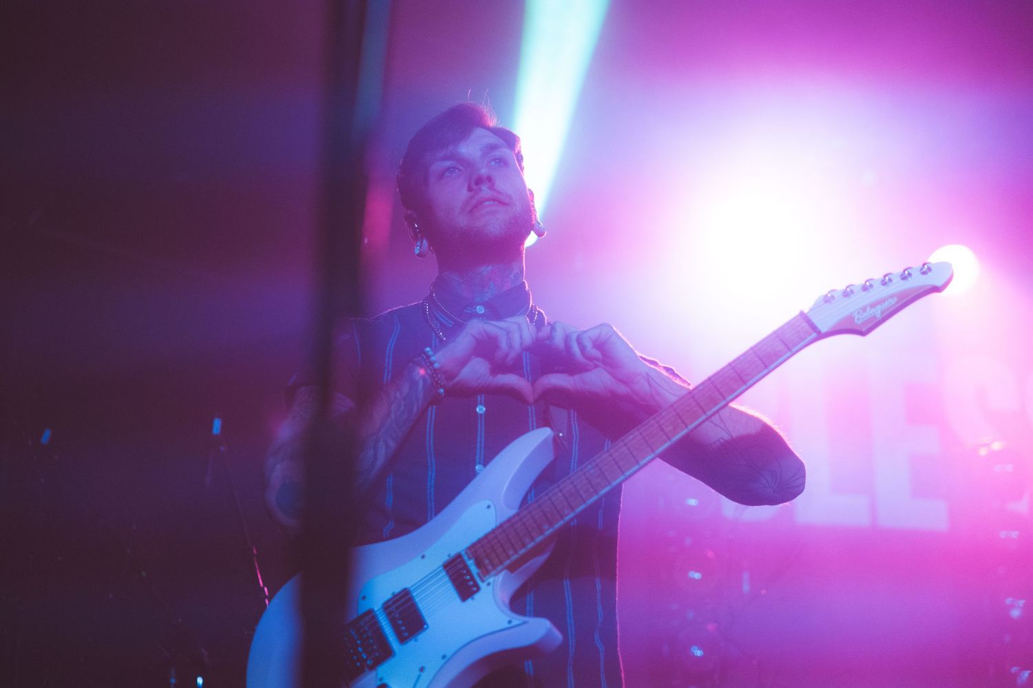 A concert guitarist performs on stage bathed in vibrant purple stage lighting during a live music performance.