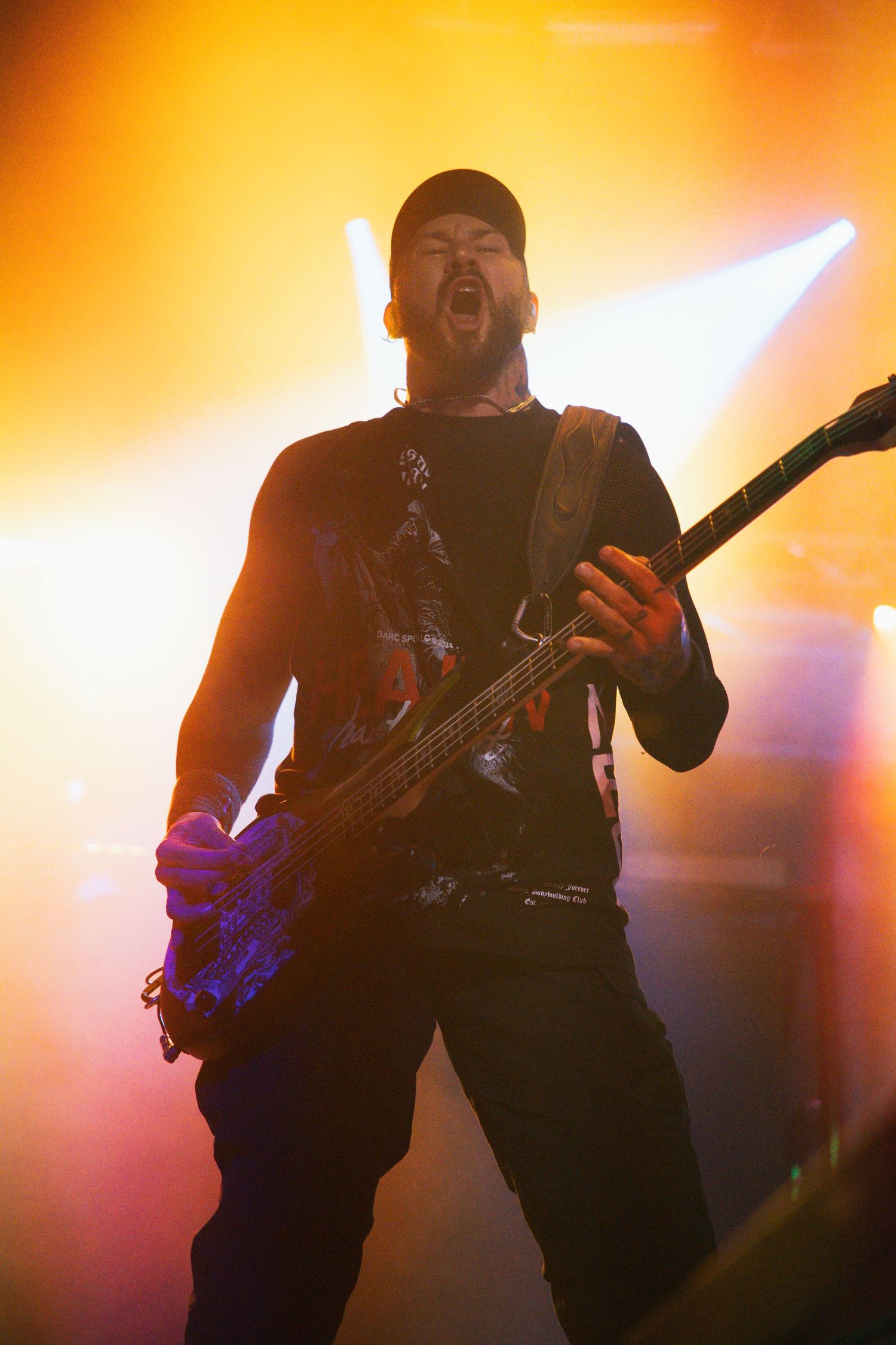 Bass guitarist performs on stage with dramatic orange lighting and fog effects during an energetic concert performance.