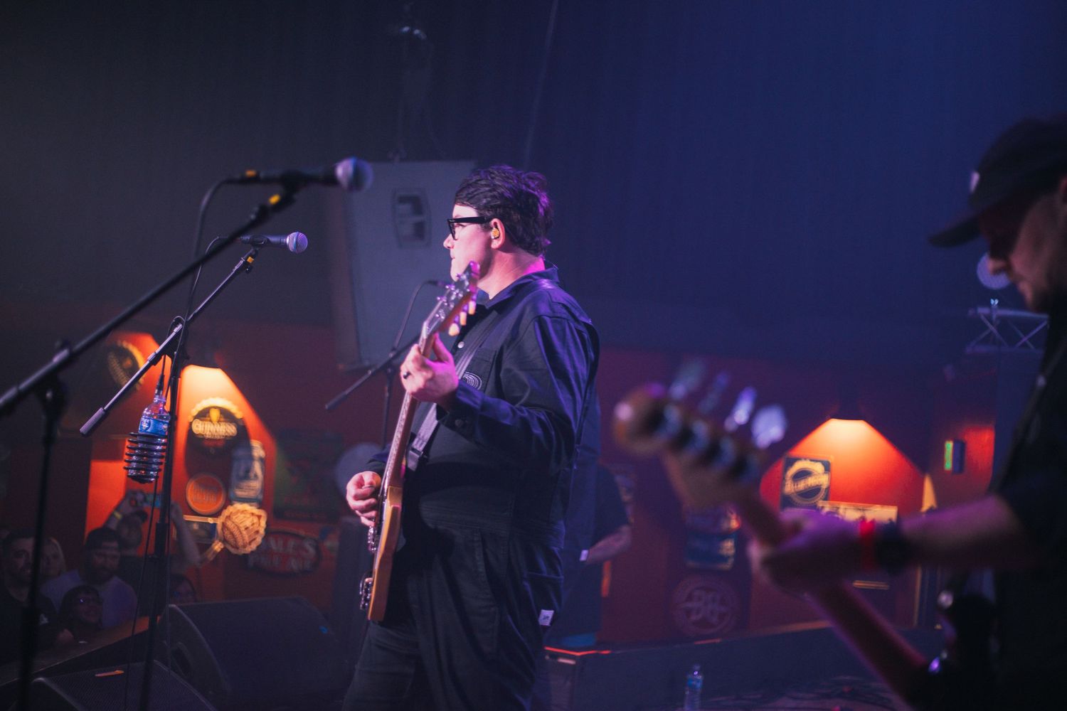 Musician playing guitar and singing into microphone with orange lights in background.