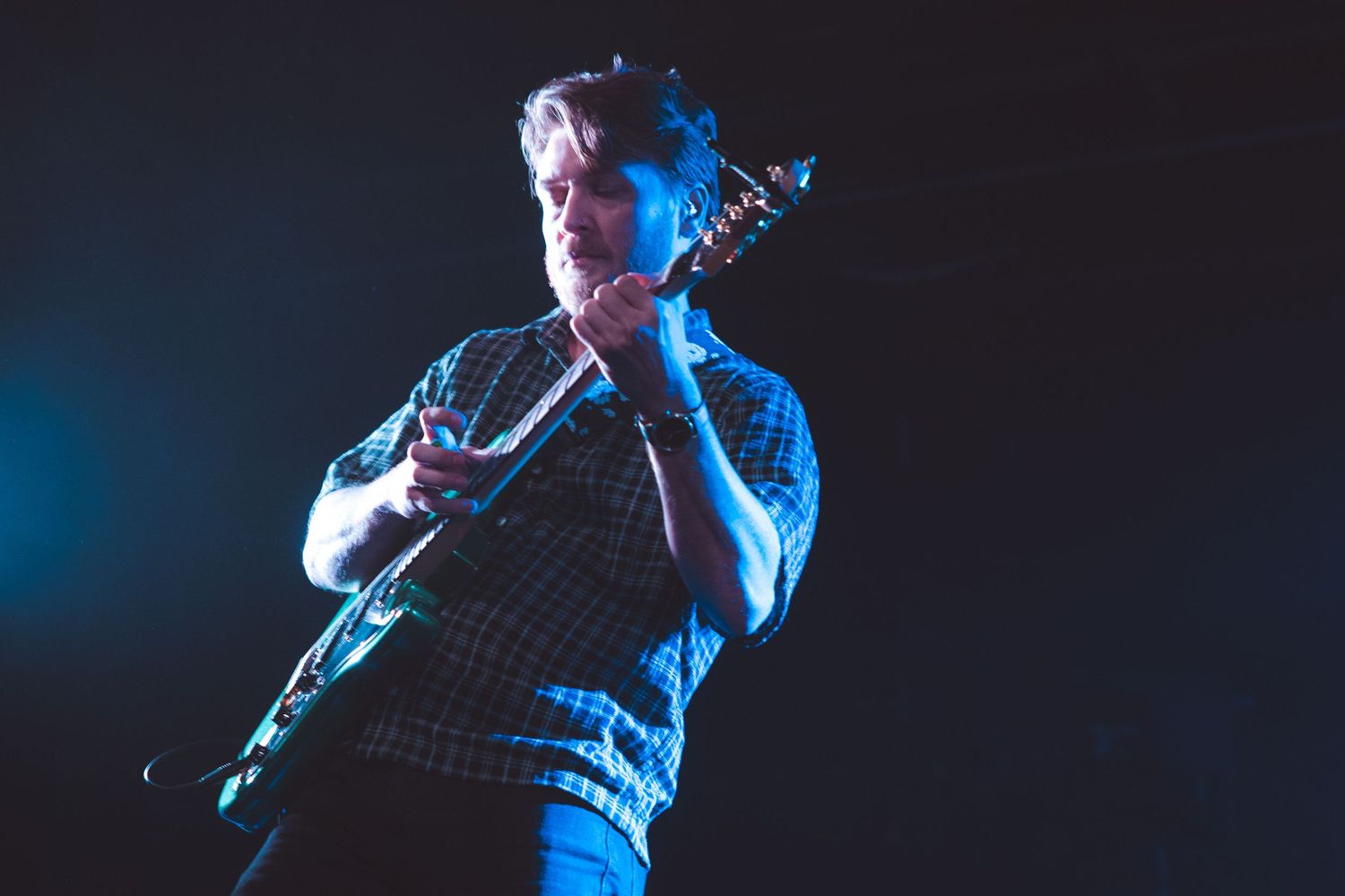 Musician performing on stage illuminated by moody blue stage lights during a concert.