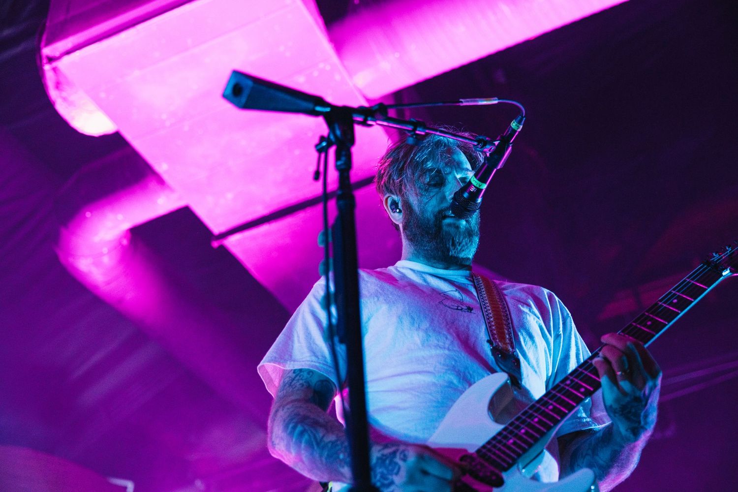 Tattooed guitarist performing on stage under vibrant purple and blue lights at a live concert.
