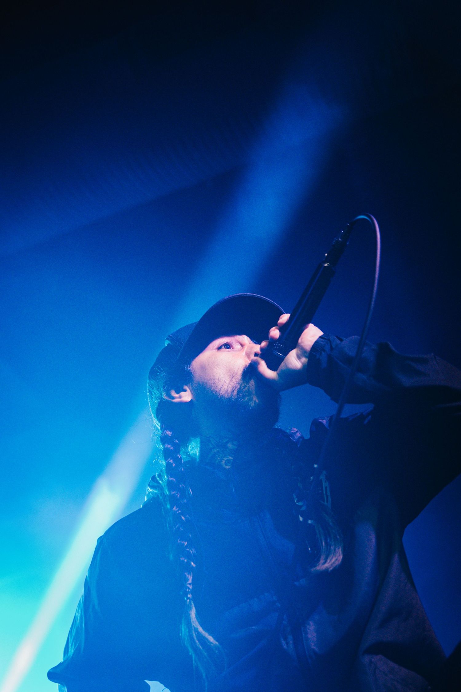 A performer in a dark outfit sings passionately on stage bathed in dramatic blue lighting during a concert performance.