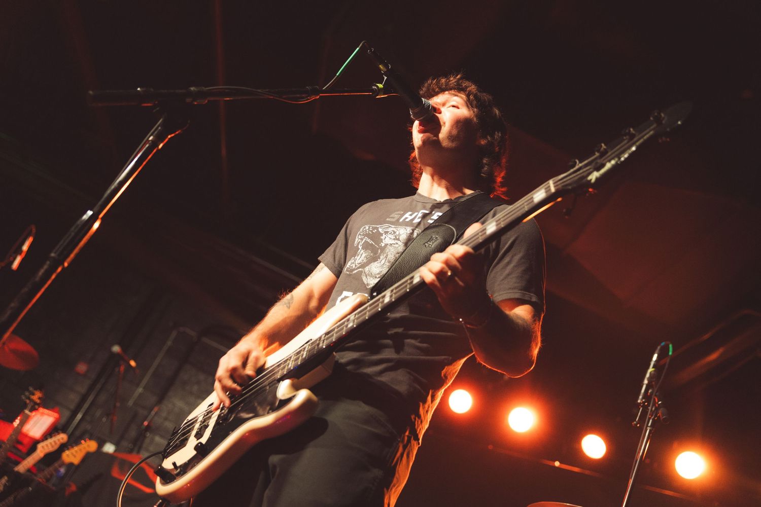Guitarist performs energetically on stage with red and orange stage lighting creating a dramatic atmosphere.