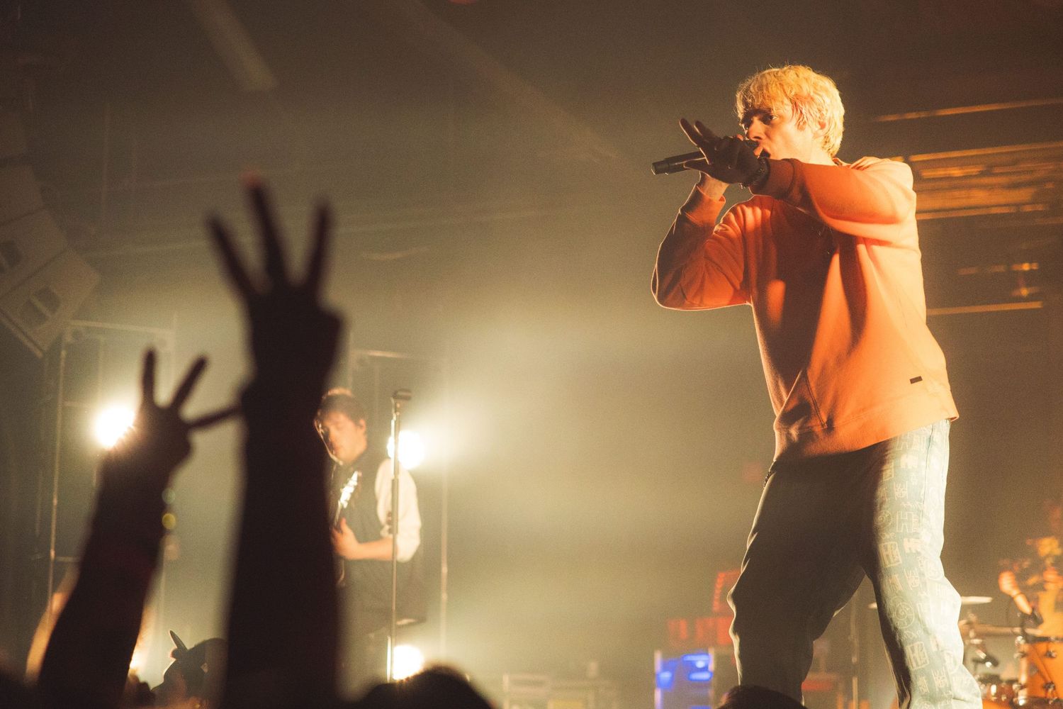 Concert crowd silhouettes with raised hands against bright stage lighting creating an energetic atmosphere.