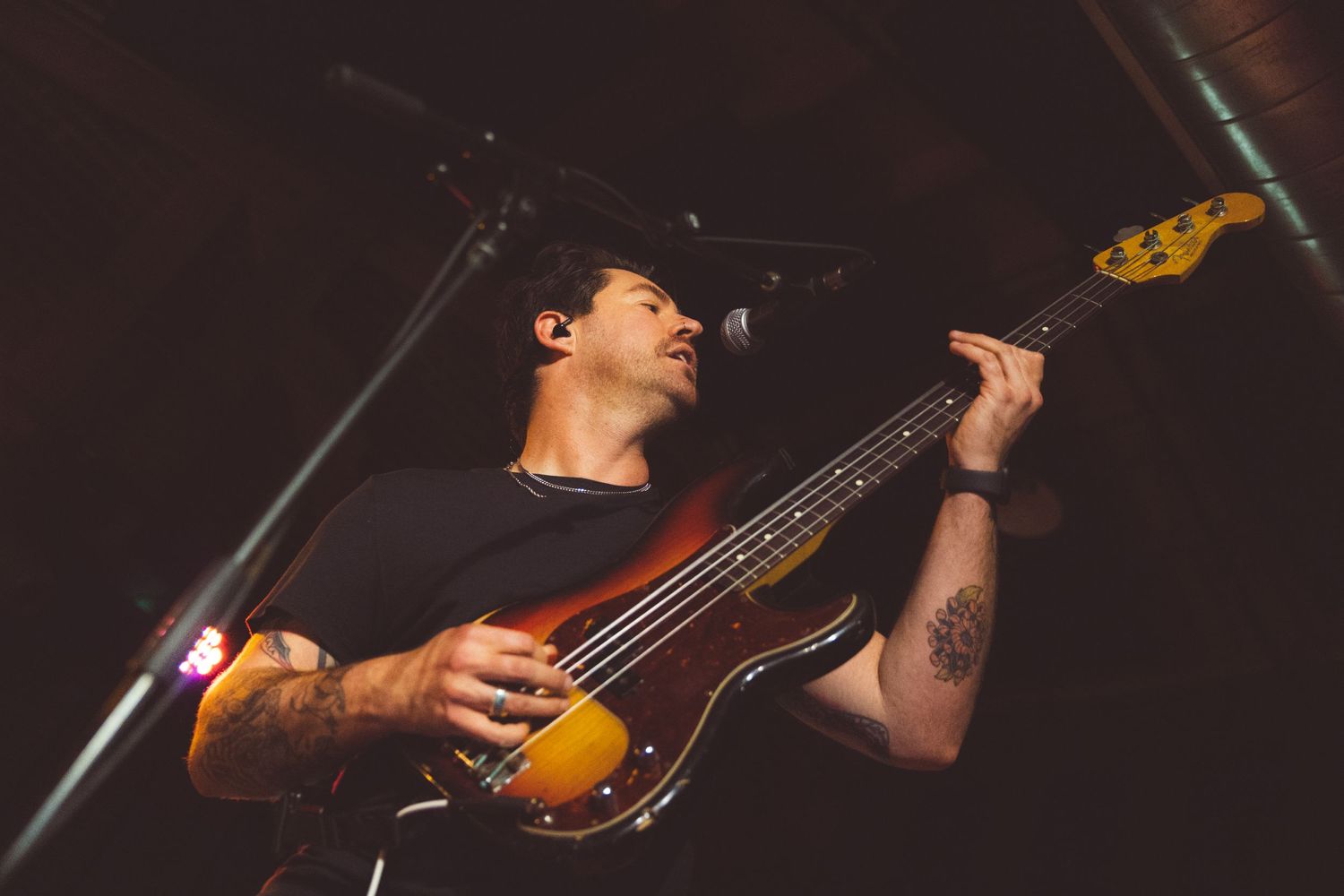 A musician plays bass guitar on stage under dramatic lighting during a live performance.