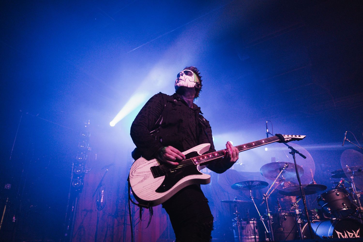 Guitarist performs on stage with electric guitar against dramatic blue lighting and fog effects during concert performance.