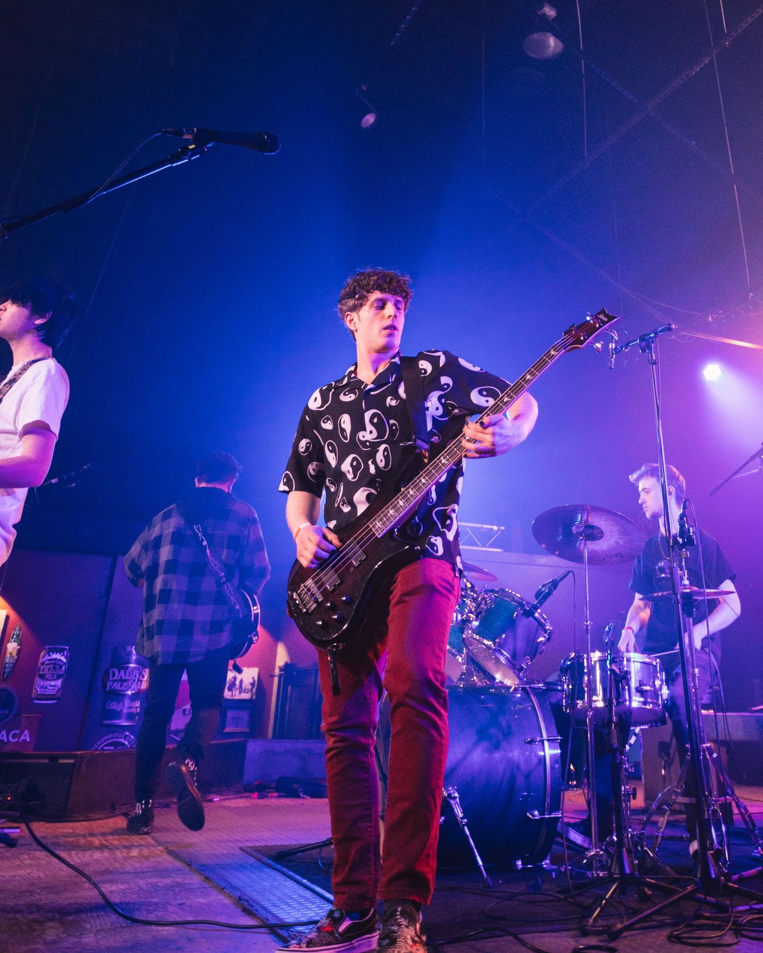 Bassist in patterned shirt and red pants performs on stage with blue lighting effects.