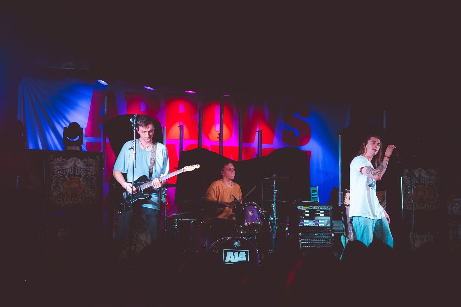 Band performs on dimly lit stage with red and blue lighting during a live music performance.