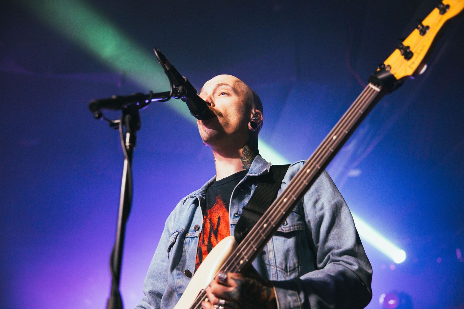 Musician wearing sunglasses performs with guitar under vibrant blue stage lighting at a concert.