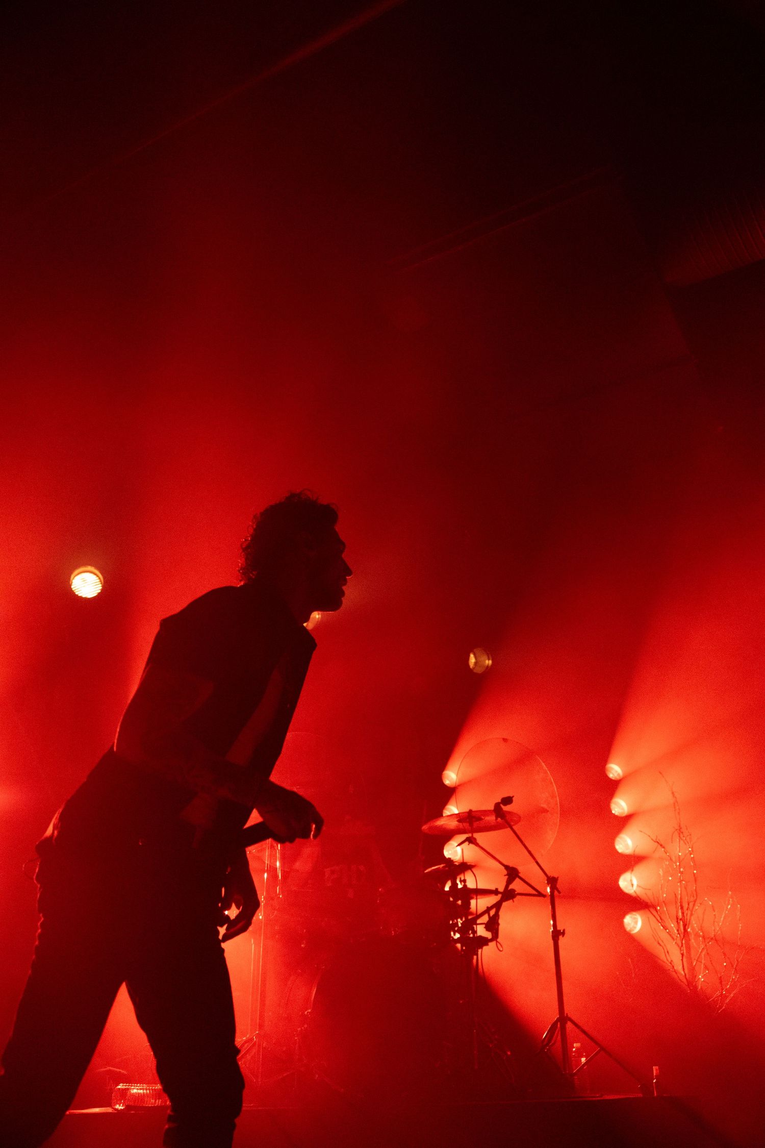 Silhouettes of musicians performing on a smoke-filled stage illuminated by intense red lighting.