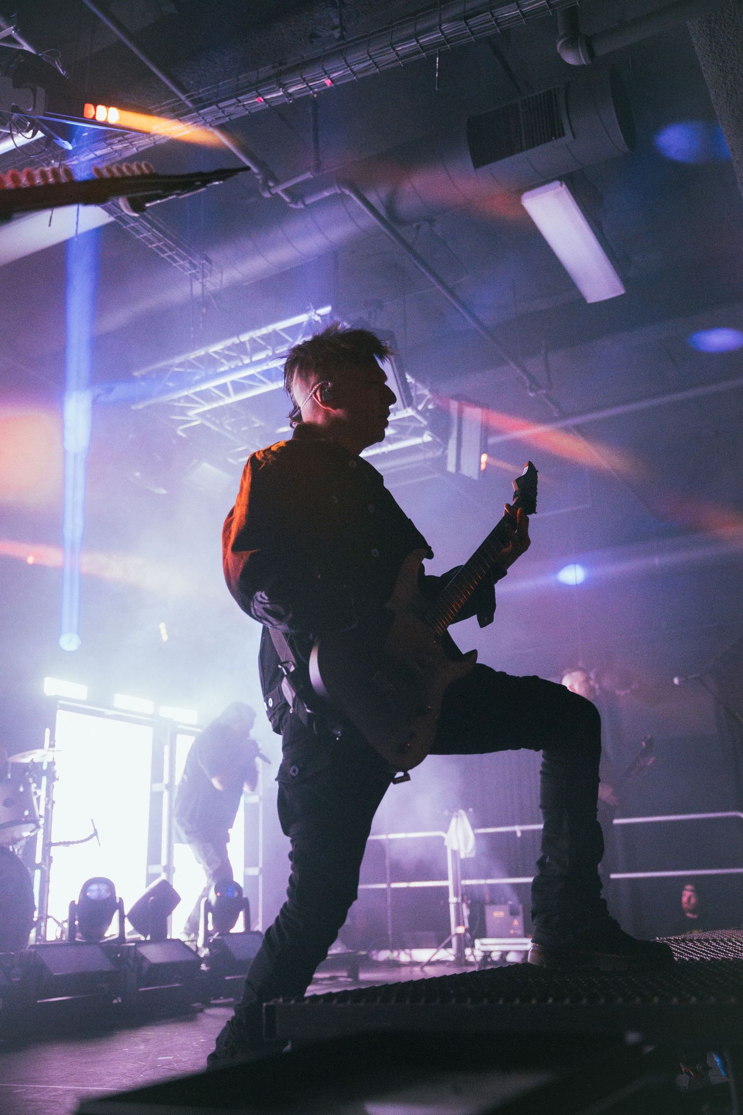 Silhouetted musician plays guitar on stage with dramatic lighting and fog effects during live concert performance.