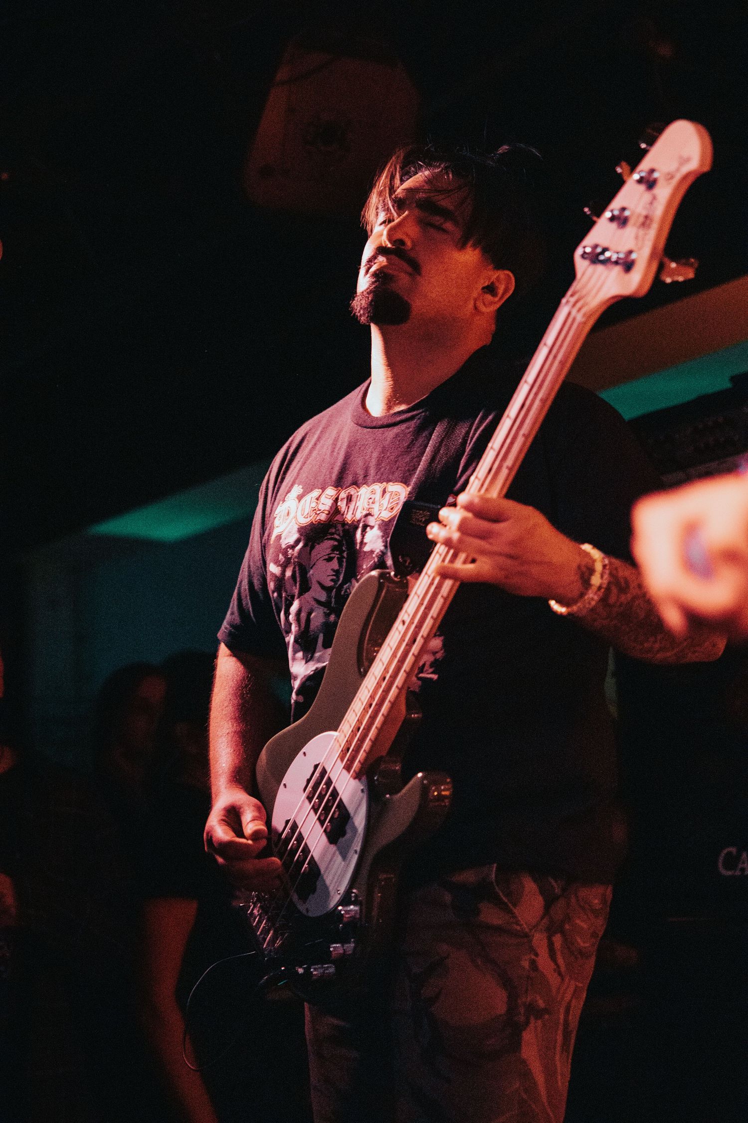 Bass guitarist in black band t-shirt passionately performs on stage under dramatic lighting.