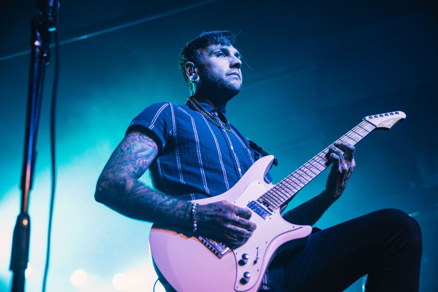 Concert performers play guitars on a stage lit with dramatic blue lighting during a live music performance.