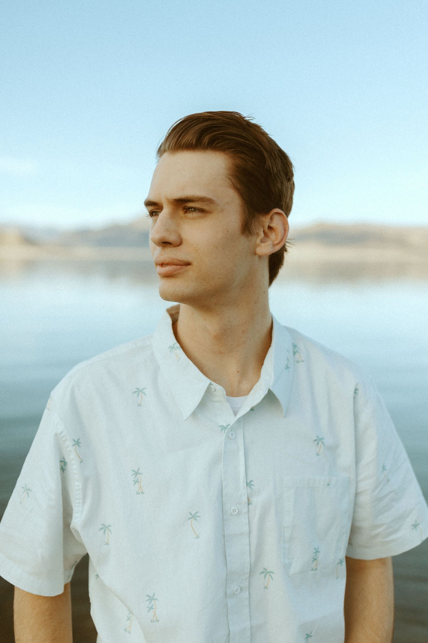 Portrait of person in white shirt against serene lakeside background at sunset.
