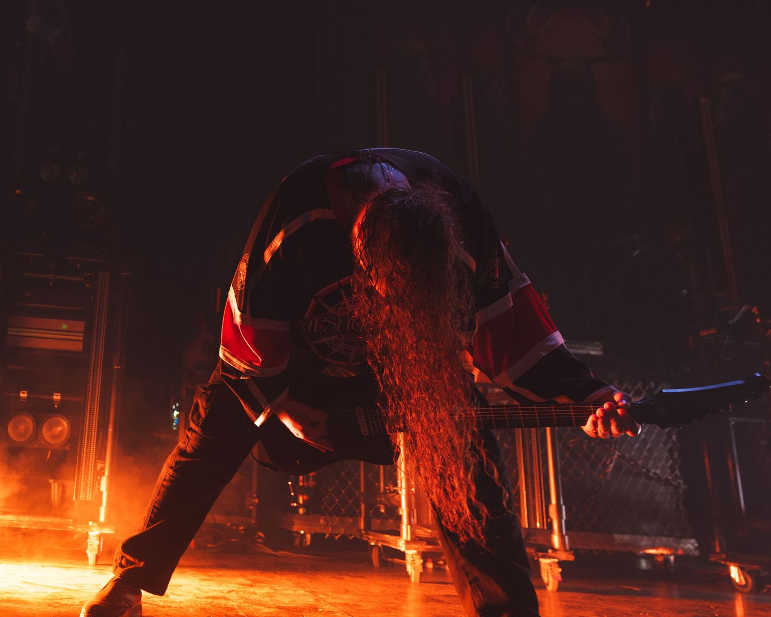Long-haired rock musician bowing on stage with dramatic red lighting during an intense live metal concert performance.