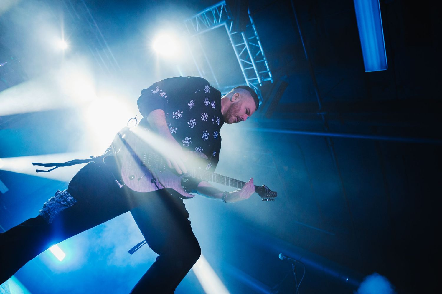 Performer wearing stars and stripes jumps energetically on stage with dramatic blue lighting behind them.