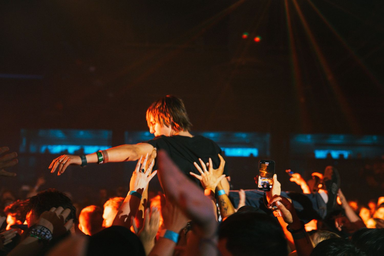 A performer crowd surfing over an audience at a concert with dramatic blue lighting in the background.