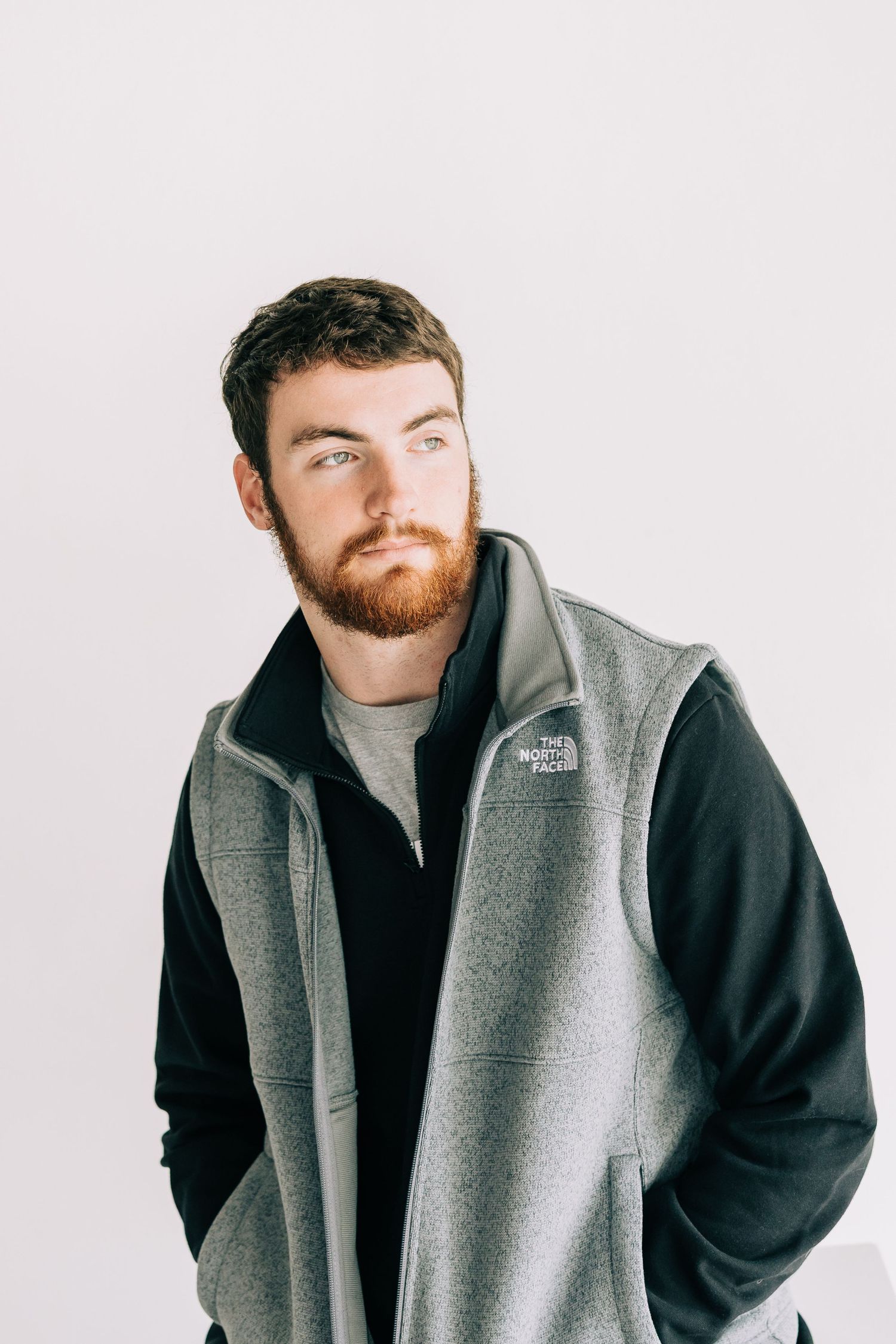 A person wearing a gray vest and black sweater poses in three similar shots against a white background.