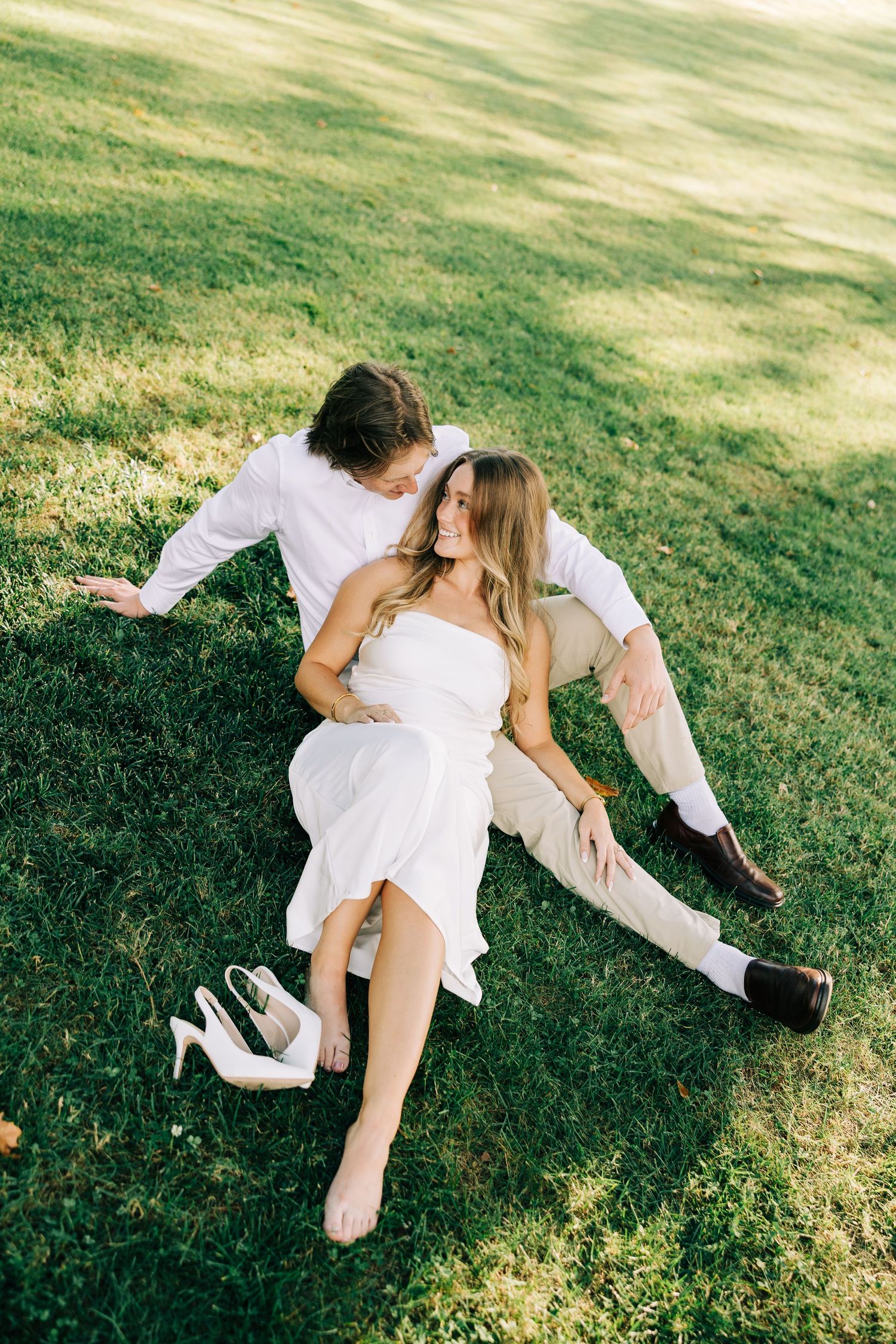 A romantic sequence of two people in white outfits rolling together on a sunny lawn.