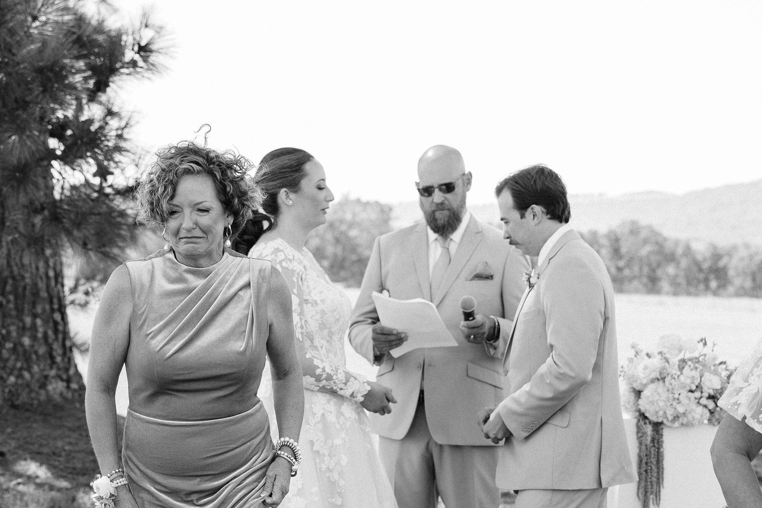 A group of wedding guests share laughter and conversation during an outdoor celebration in black and white.