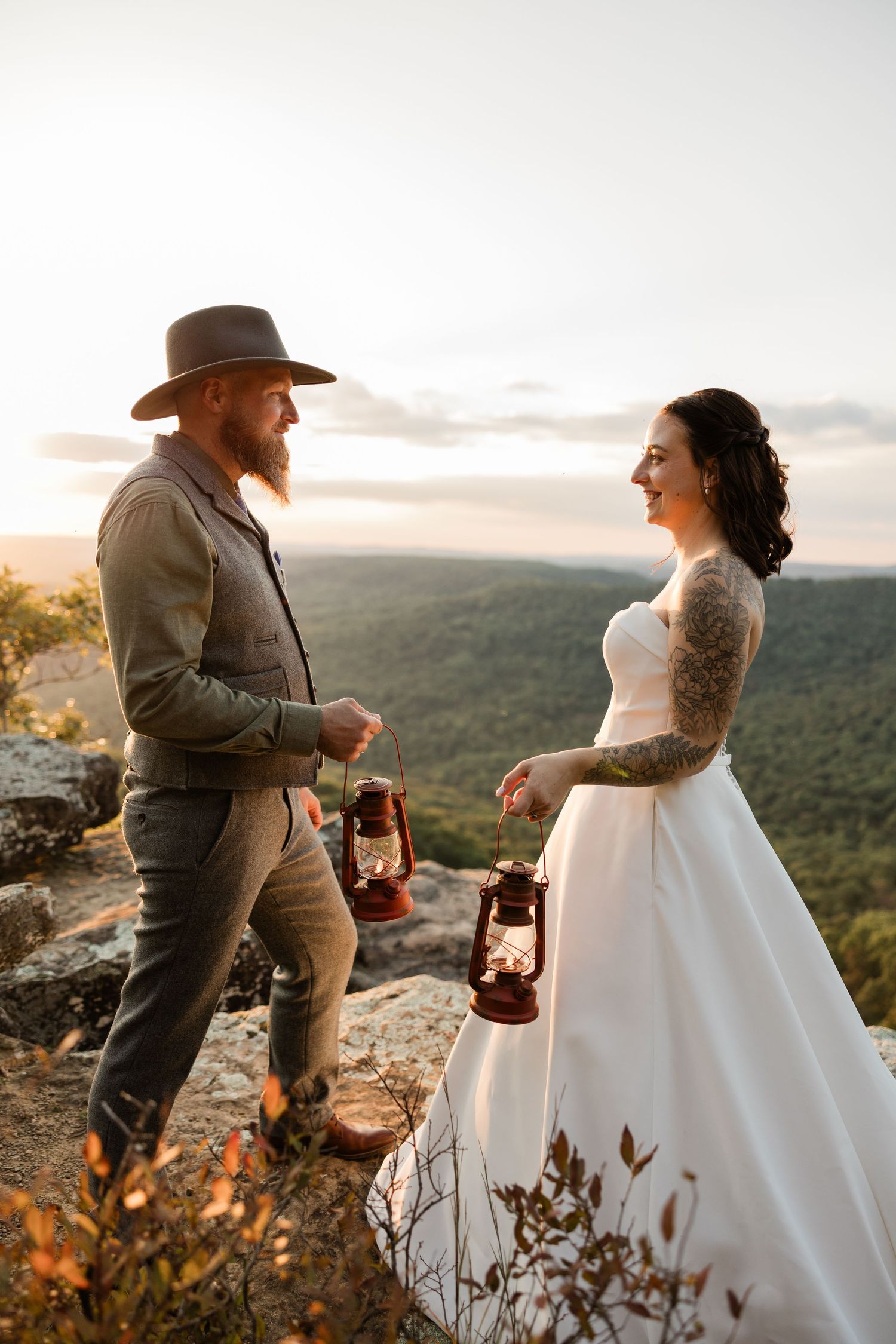 A couple shares a romantic moment on a mountaintop during sunset while holding lanterns.