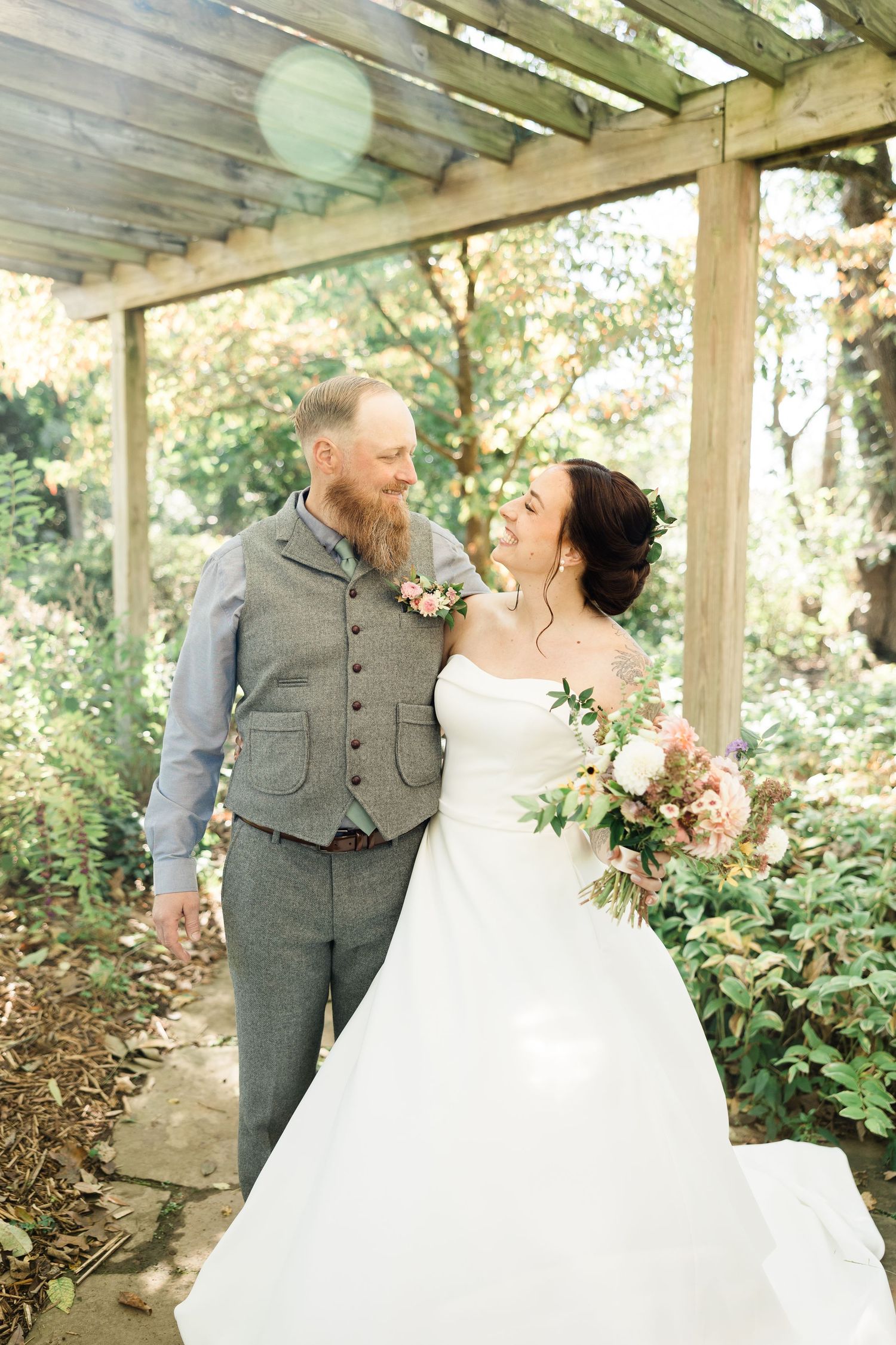 Wedding couple shares romantic moments under a rustic wooden pergola surrounded by greenery.