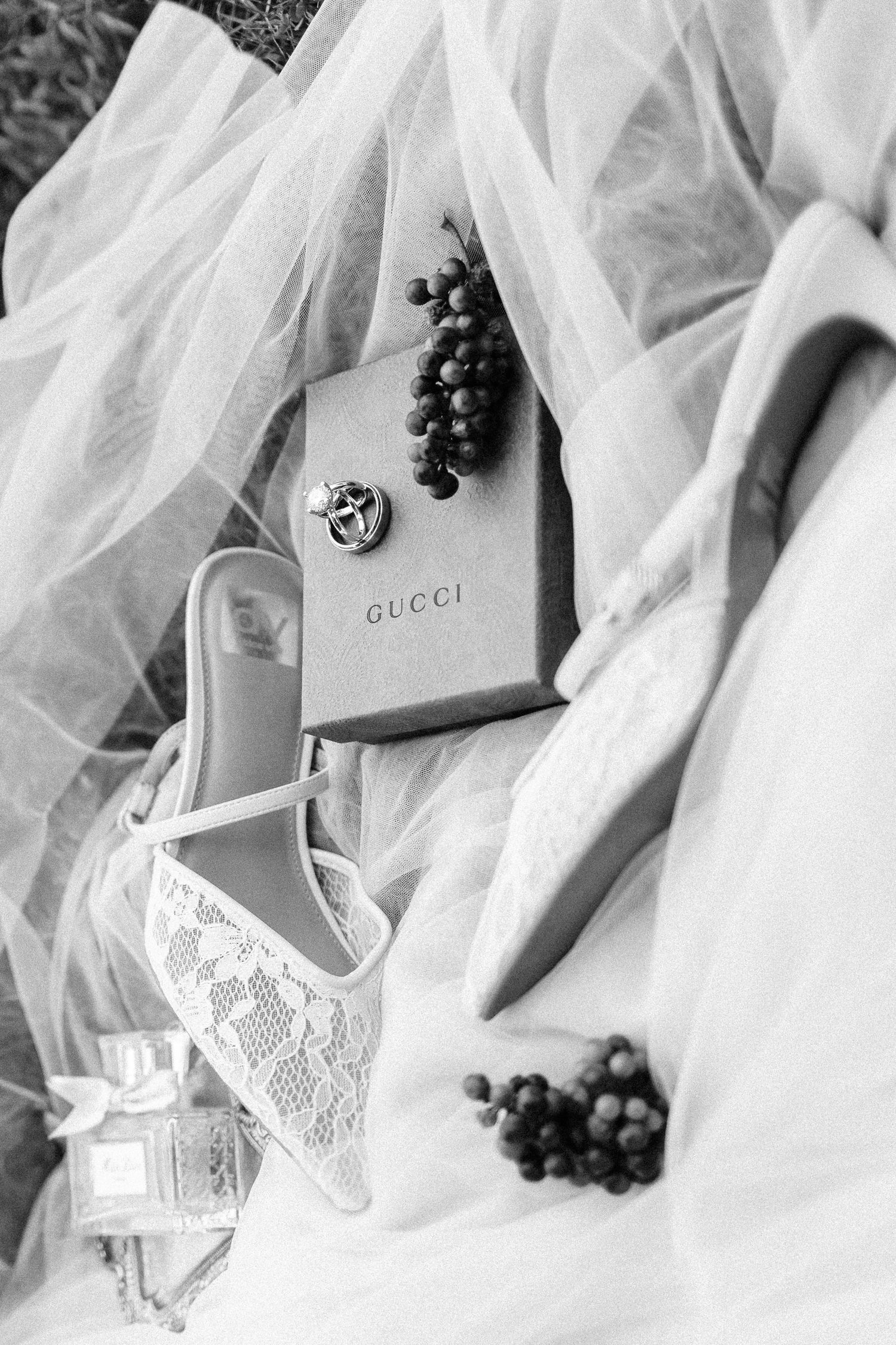 Elegant wedding details featuring white tulle fabric, Gucci accessories, and dark grapes in a romantic composition.