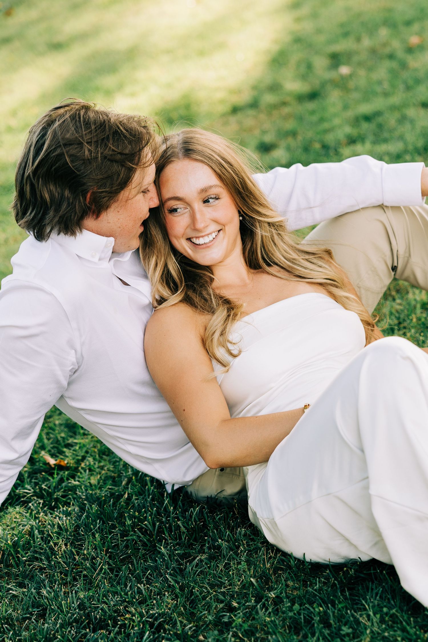 A couple in white clothing lying together on green grass in a romantic outdoor photoshoot series.