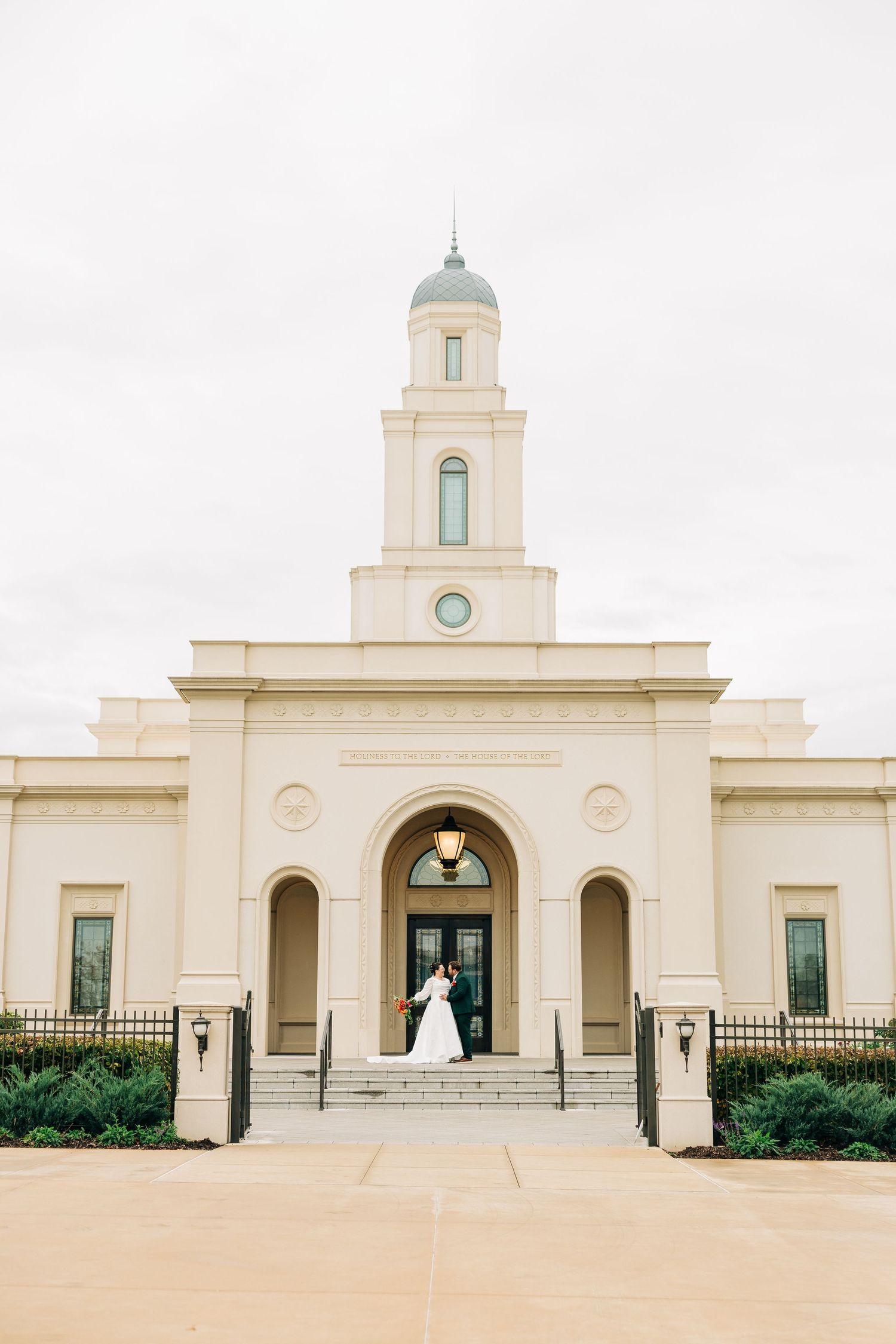 Modern white church building with bell tower and symmetrical architecture against cloudy sky.