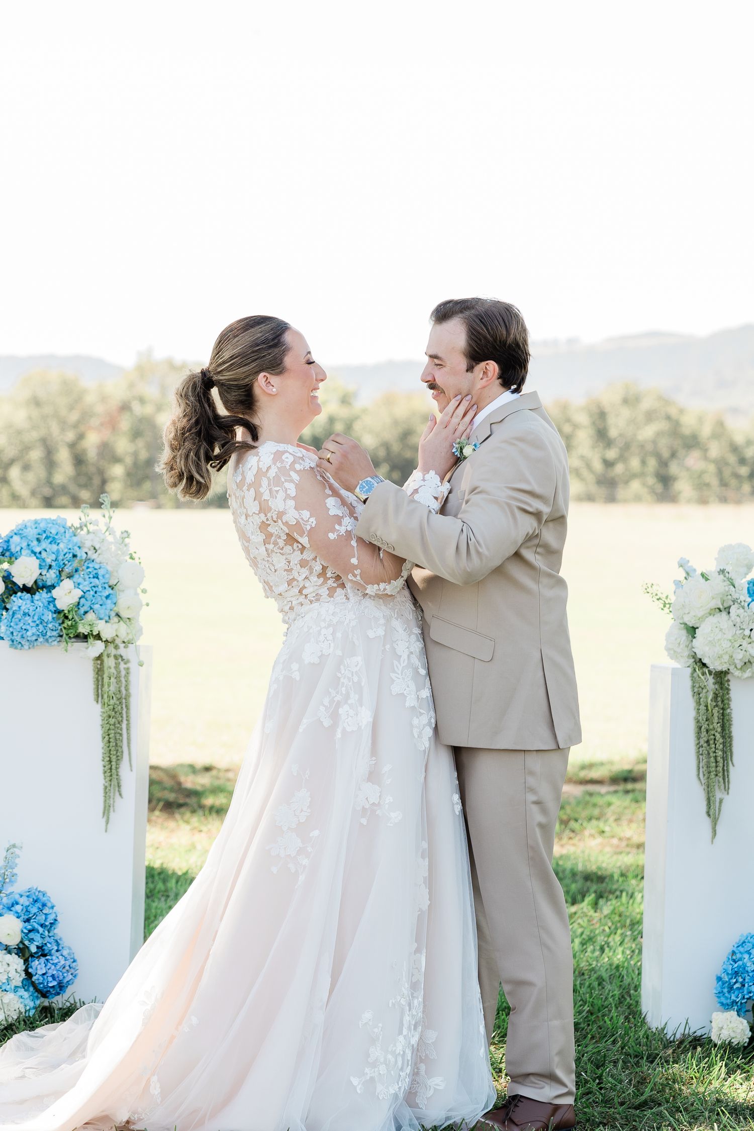 Couple sharing emotional moment at outdoor wedding ceremony with blue and white floral decorations.