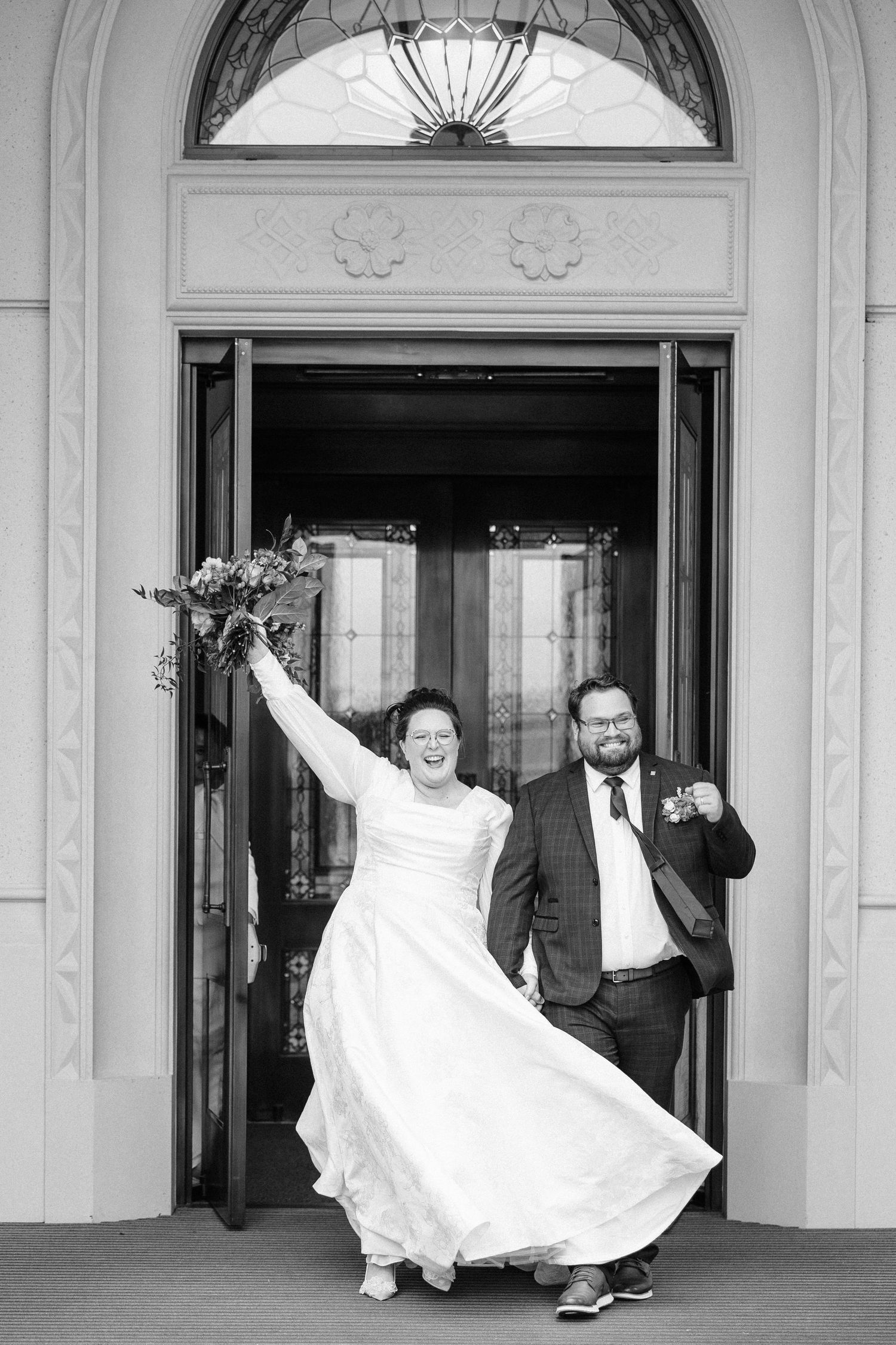 Black and white series showing playful wedding moments in an elegant hallway with arched doorways.