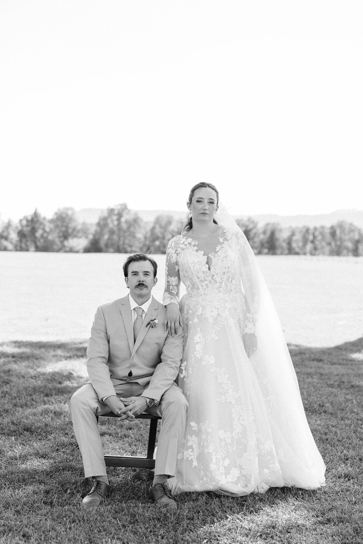 Black and white portrait of a couple sitting on a bench in a scenic outdoor setting.