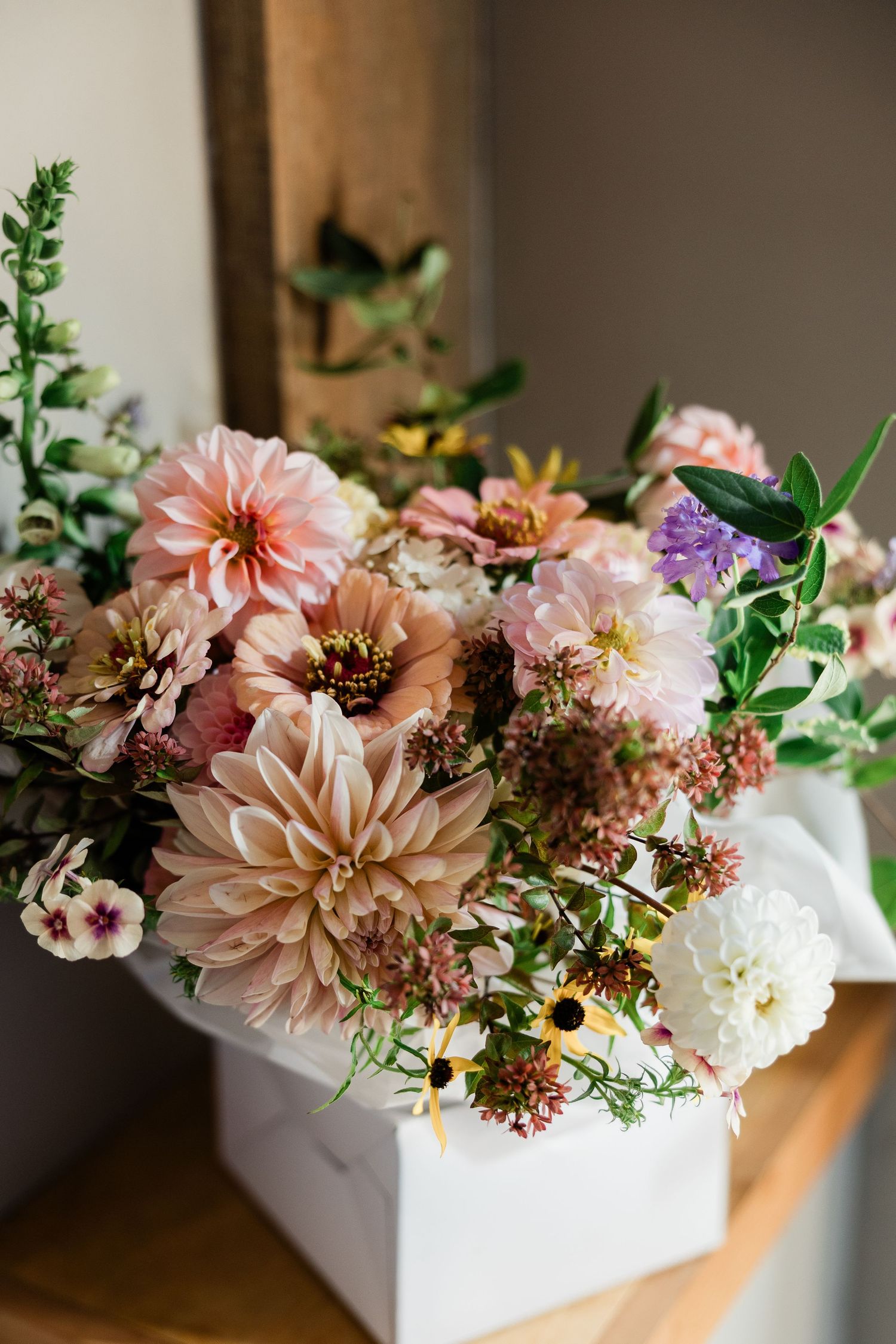 Romantic floral arrangement featuring pink dahlias, white flowers, and greenery in a white rectangular vase.